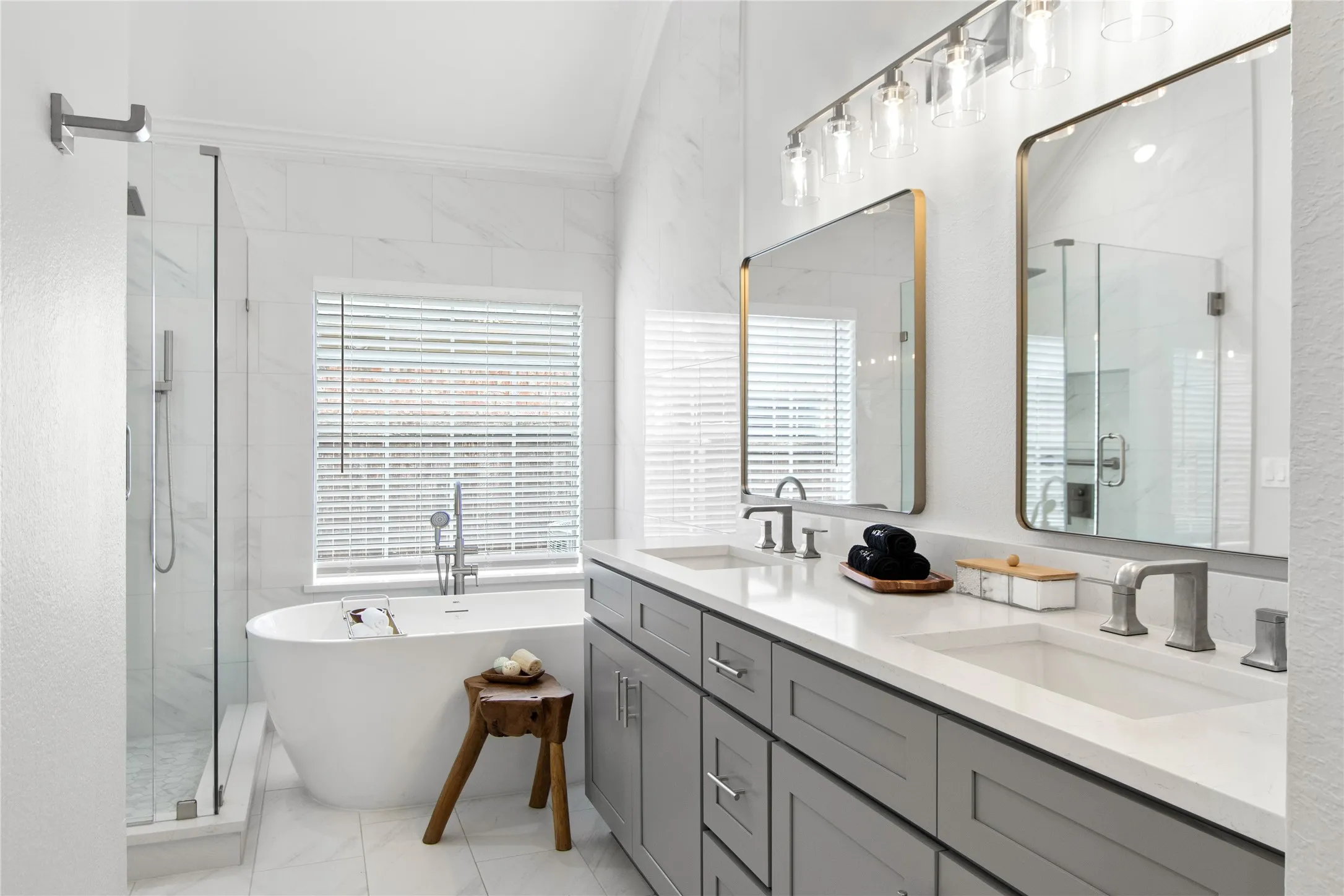 Bathroom featuring a freestanding soaking tub, frameless glass shower enclosure, dual vanity with undermount sinks, and a multi-light fixture