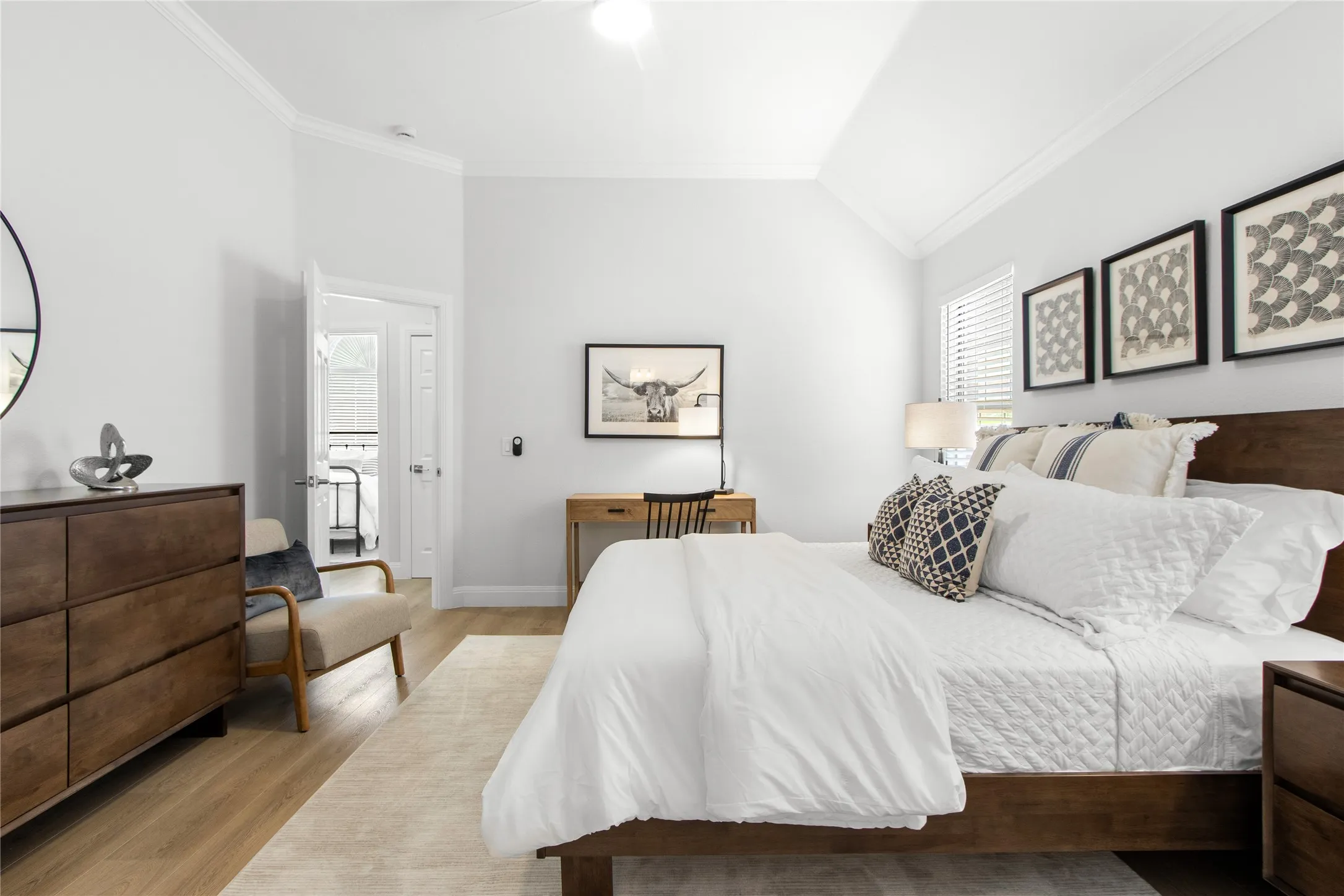 Spacious bedroom featuring vaulted ceilings, crown molding, wood-finish flooring, and a double-door entry