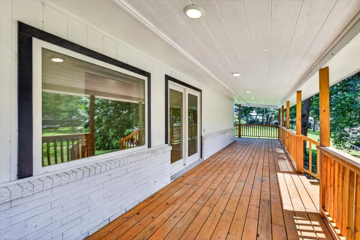 Expansive covered porch featuring wood-finish decking, natural wood railings, and recessed ceiling lighting