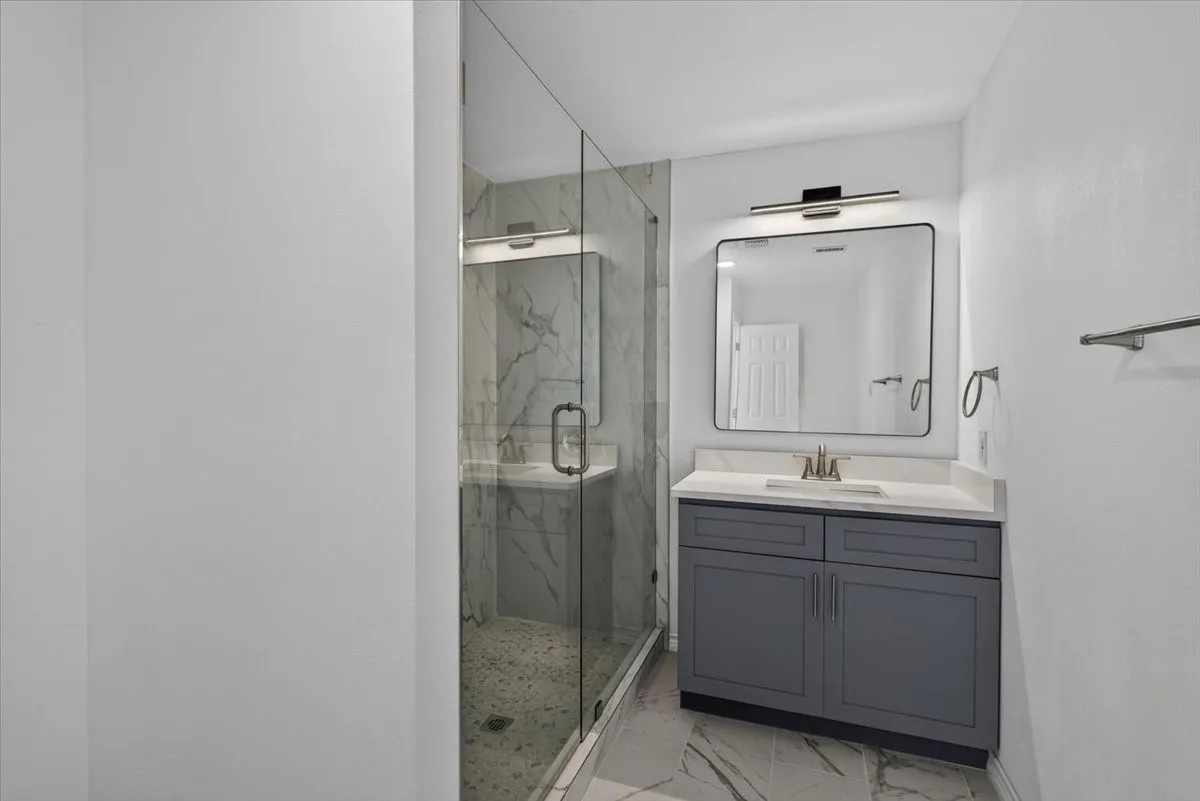 Contemporary bathroom featuring a frameless glass shower enclosure, a single vanity with a gray cabinet base, and a white countertop