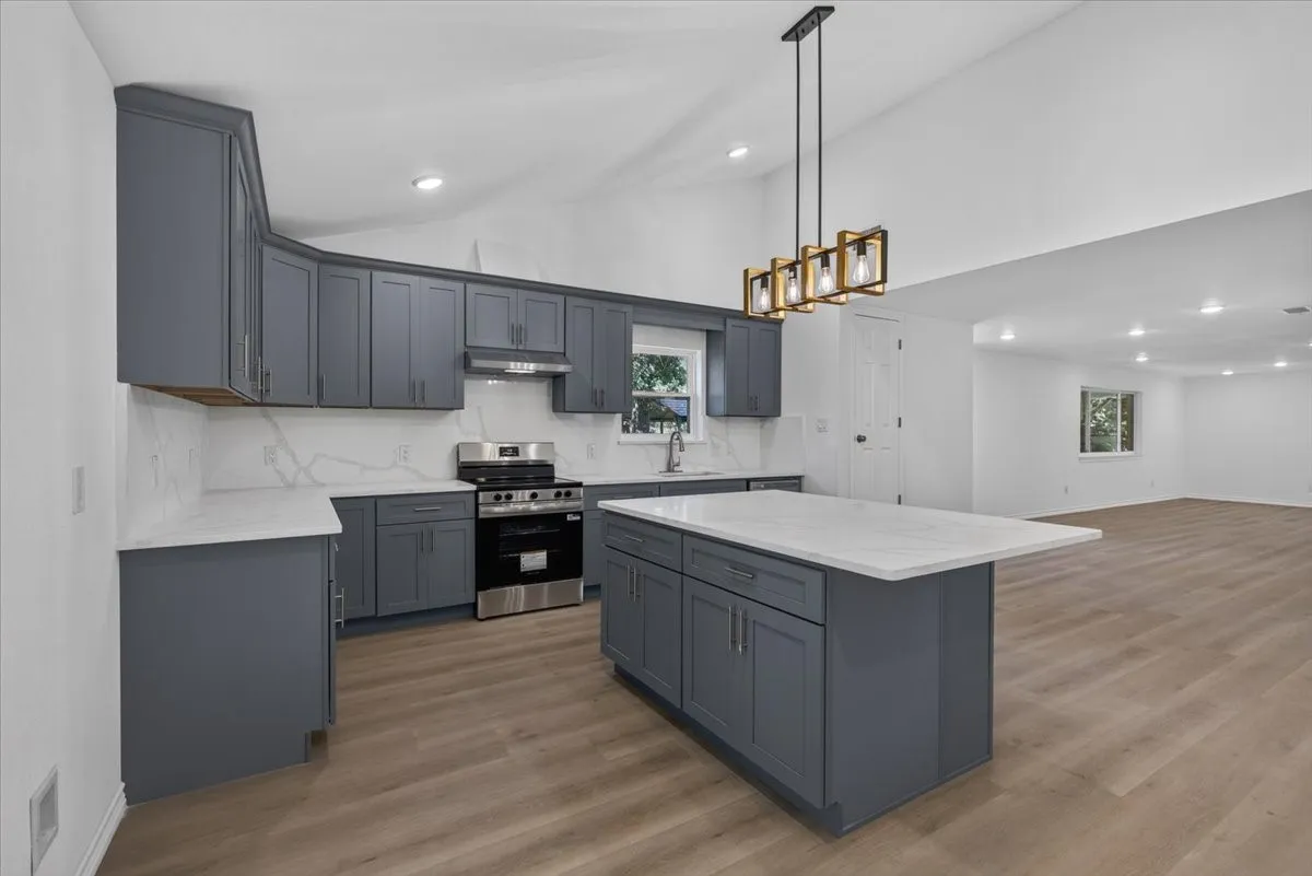 Kitchen featuring dark grey cabinetry, white countertops with veining, a stainless steel range, and a central island