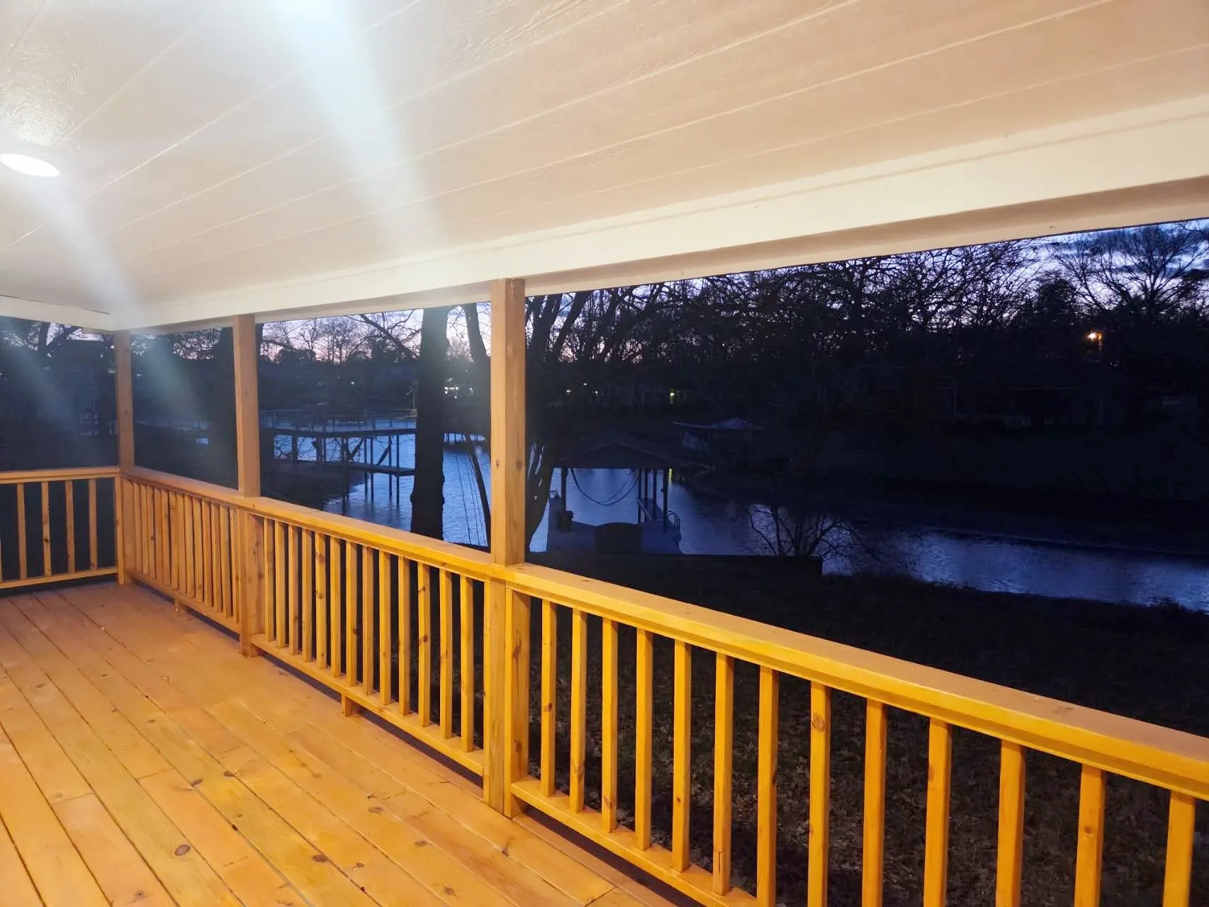 Covered rear porch with natural wood flooring and railings, overlooking waterfront scenery