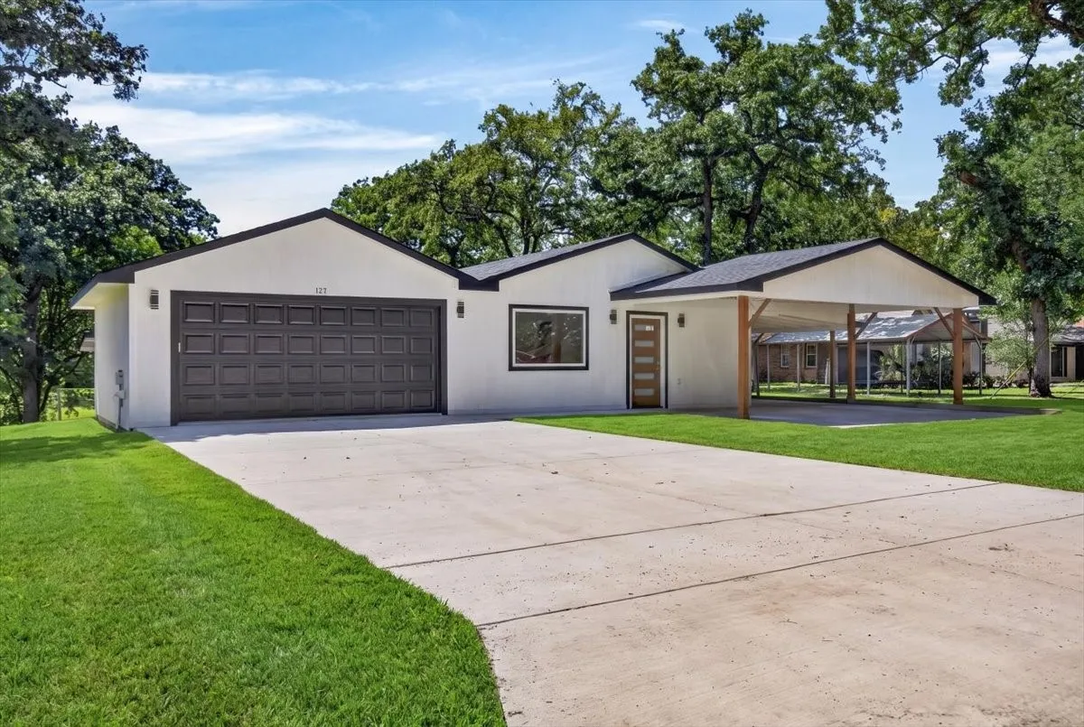 Modern single-story residence featuring a two-car garage, a covered carport, and a light-toned exterior with dark trim
