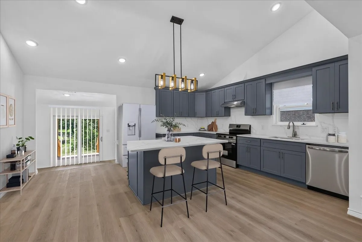 Kitchen featuring vaulted ceiling, recessed lighting, wood-finish flooring, custom cabinetry, and stainless steel appliances