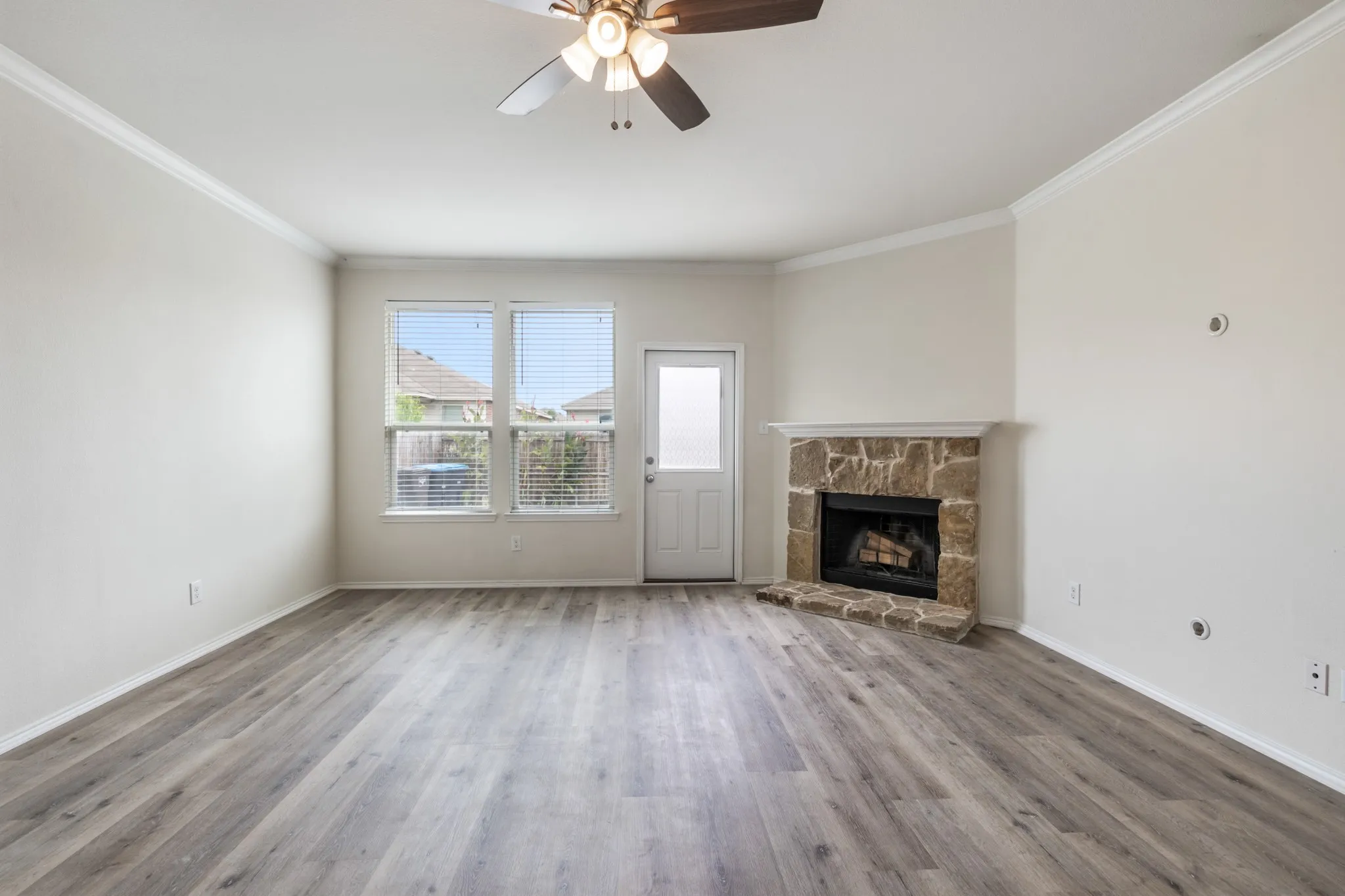 Spacious living area featuring wood-finish flooring, a corner fireplace with a stone surround, and multiple windows
