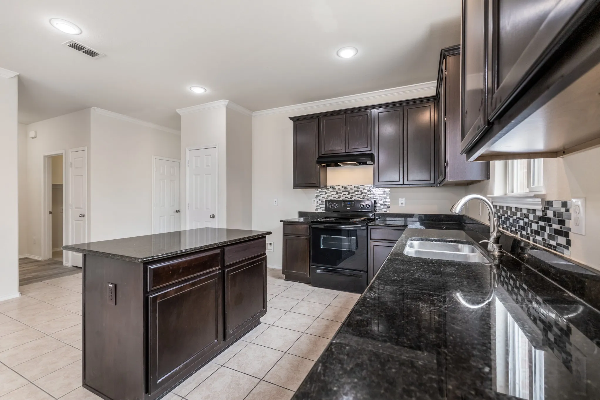 Kitchen featuring a central island with cabinetry, dark wood-finish cabinetry, black countertops, a mosaic tile backsplash, and recessed lighting