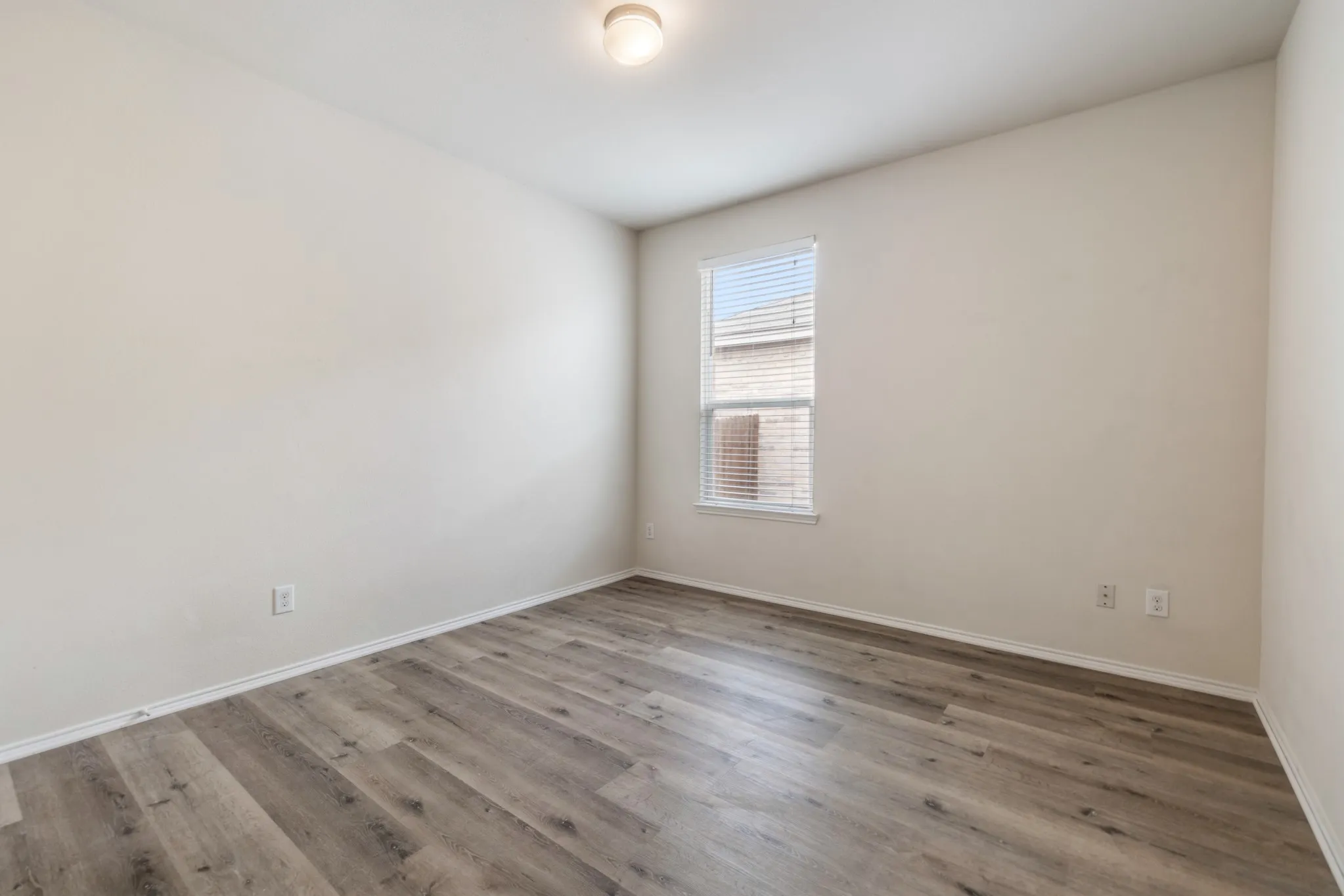 Neutral tone walls featuring wood-finish flooring, a window with blinds, and a ceiling-mounted light fixture