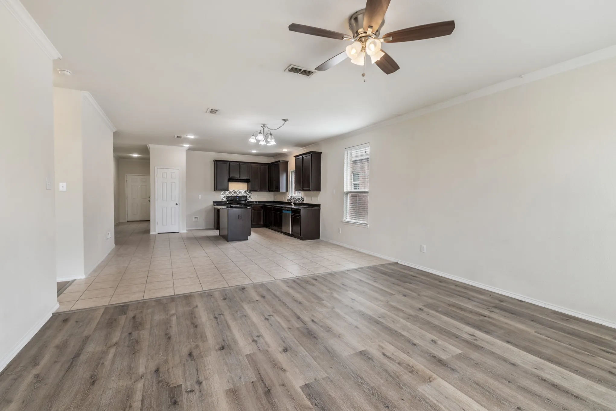 Open-concept living area featuring wood-finish flooring, a ceiling fan with integrated lighting, and a light-filled window