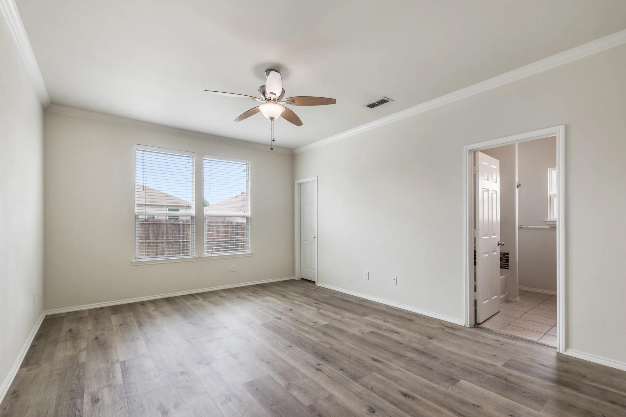 Spacious room featuring wood-finish flooring, a ceiling fan with light fixture, and two windows with blinds
