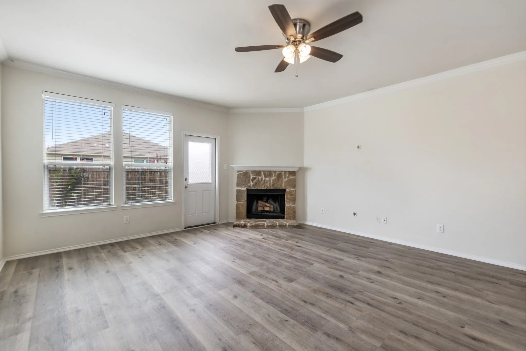 Spacious room featuring wood-finish flooring, a stone fireplace, and a ceiling fan with integrated lighting
