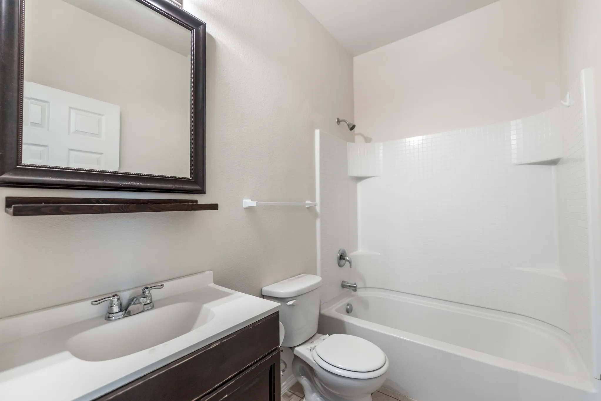 Bathroom featuring a white bathtub with a shower, a dark wood-finish vanity with an integrated sink, a framed mirror, and a white toilet