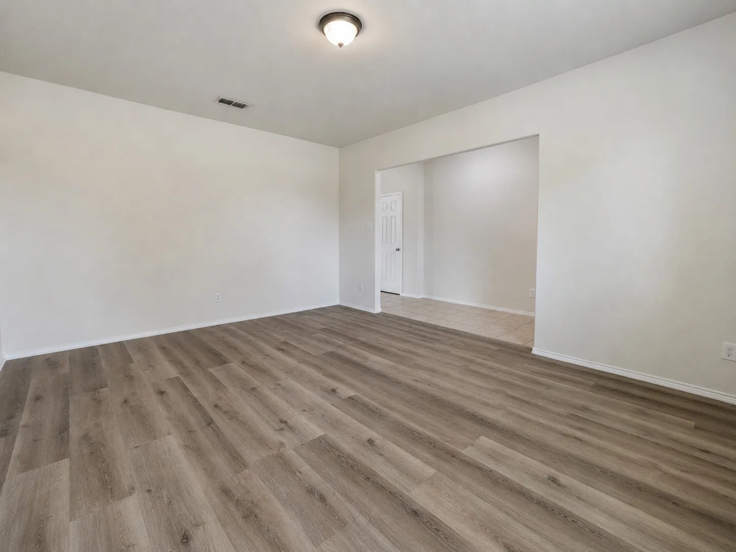 Spacious room featuring wood-finish flooring, light-colored walls, and a ceiling-mounted light fixture
