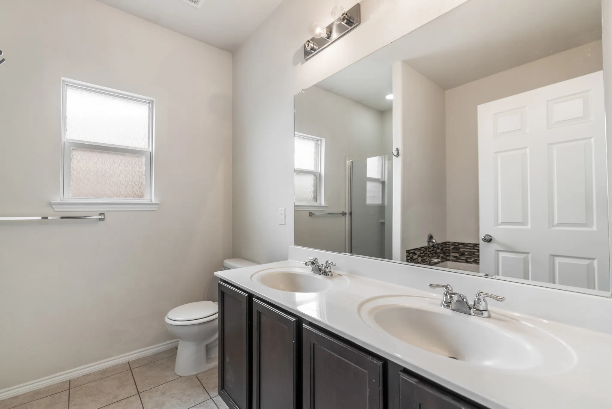 Bathroom featuring a dual vanity with dark wood-finish cabinetry and white countertops, chrome fixtures, tile flooring, and a privacy window