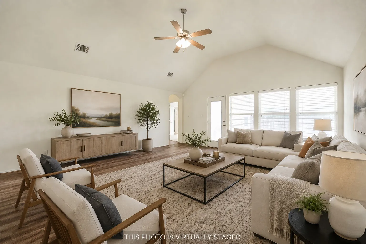 Spacious living room featuring a vaulted ceiling with a ceiling fan, wood-finish flooring, and multiple large windows with blinds. (virtually staged furniture, blinds are real.)