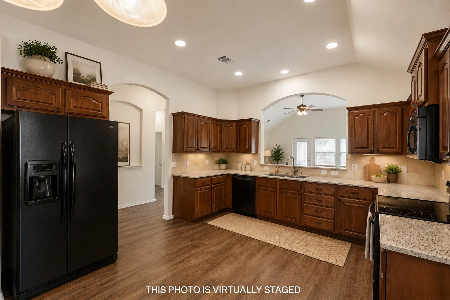 Spacious kitchen featuring wood-finish flooring, warm-toned cabinetry, light-colored countertops, recessed lighting, and a window above the sink