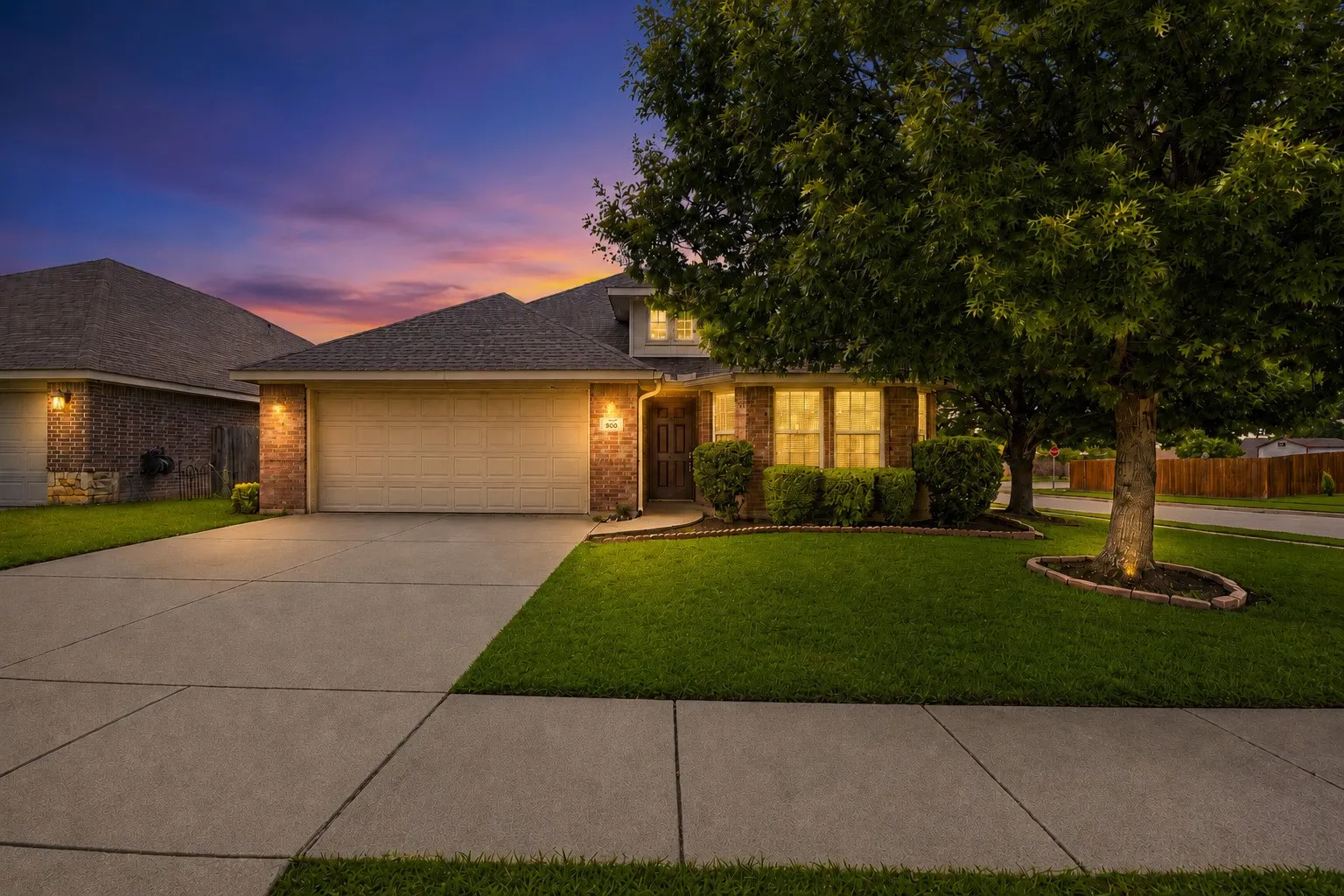 Brick facade home featuring an attached two-car garage, concrete driveway, and front yard with mature trees