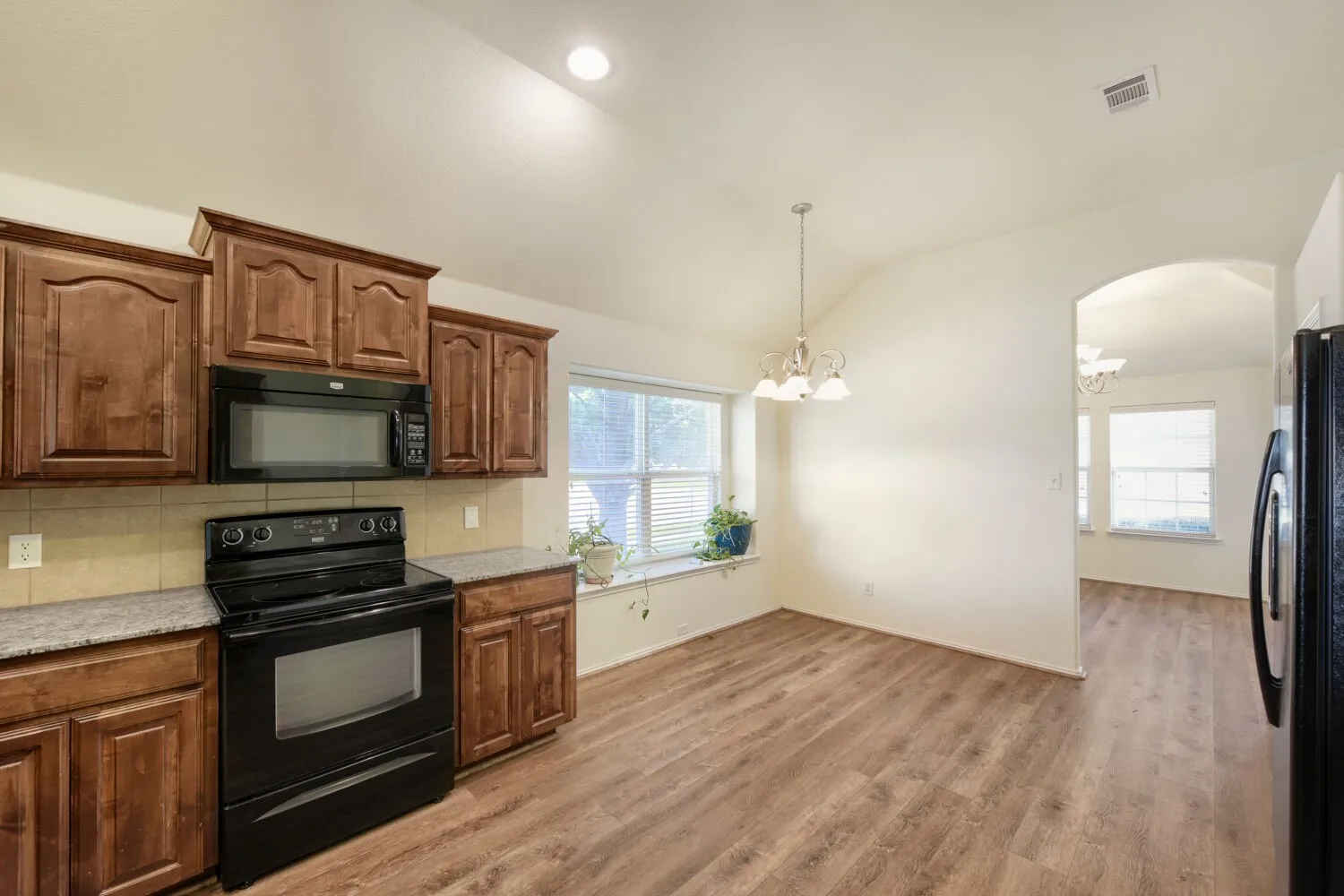 Kitchen and dining area featuring wood-finish flooring, wood cabinetry, built-in microwave, and a black electric range