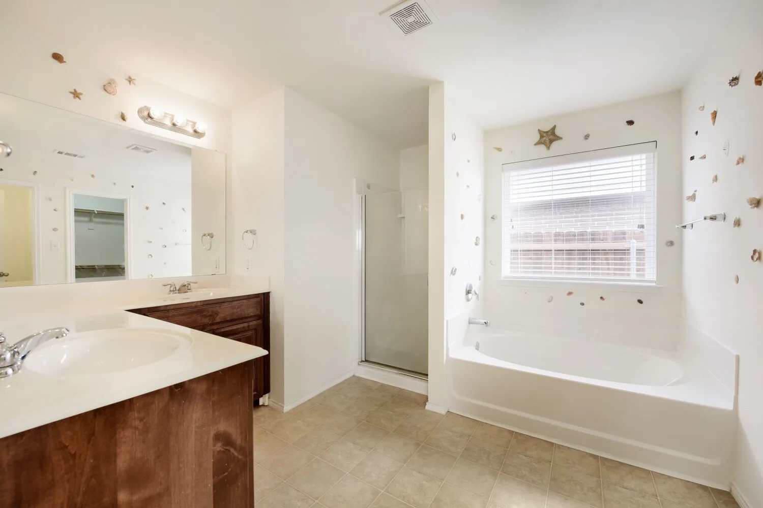 Bathroom featuring a double vanity with wood-finish cabinetry and integrated sinks, a built-in soaking tub, a separate glass-enclosed shower, and tiled flooring