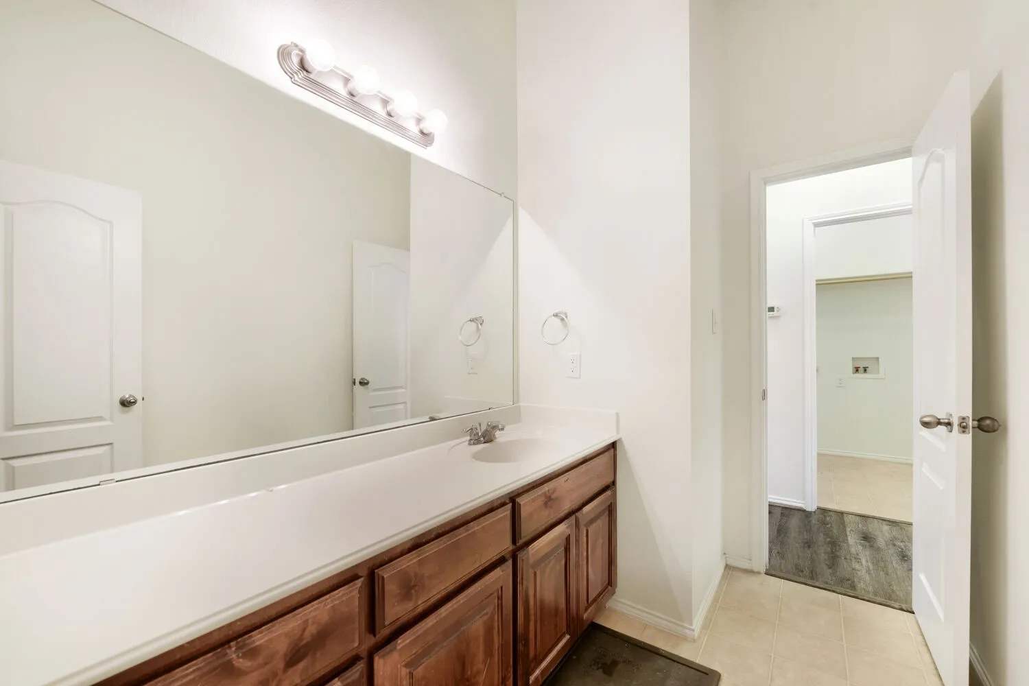 Bathroom vanity featuring a long countertop, single sink, and substantial mirror with overhead lighting