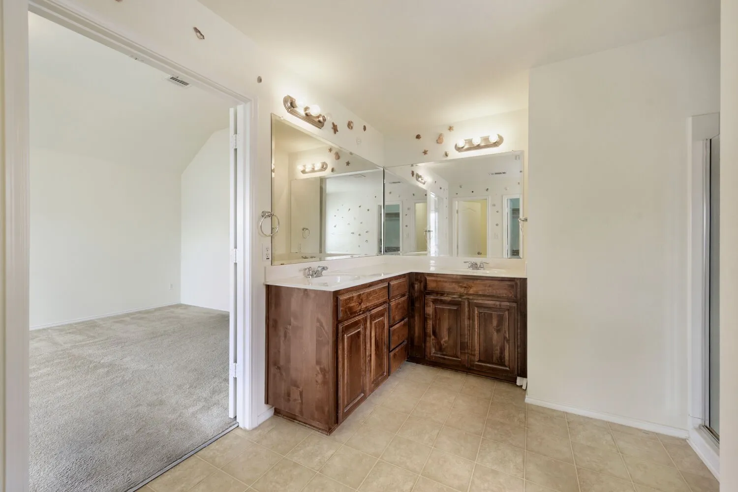 Bathroom featuring dual vanity with wood cabinetry, light-toned countertops, and wall-mounted light fixtures