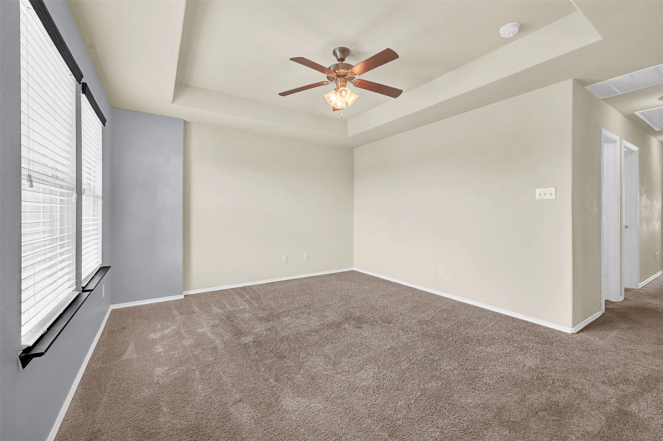 Spacious room featuring tray ceilings, neutral wall tones, and plush carpeting