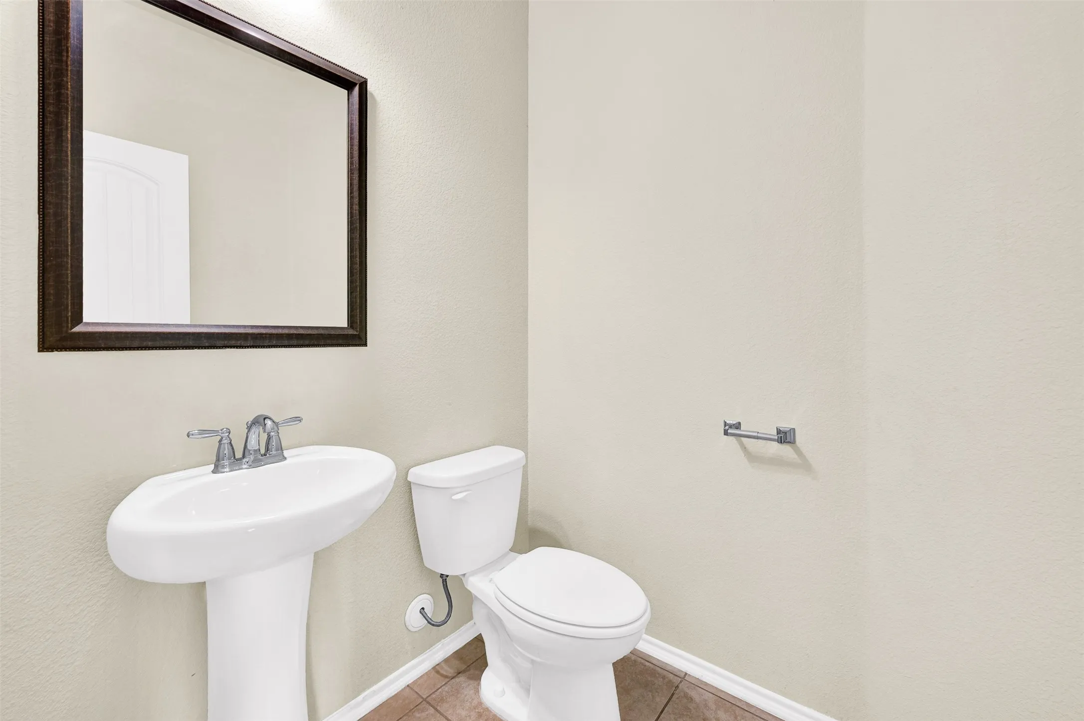 Powder room featuring a pedestal sink with chrome fixtures, a framed wall mirror, a white toilet, and neutral wall paint