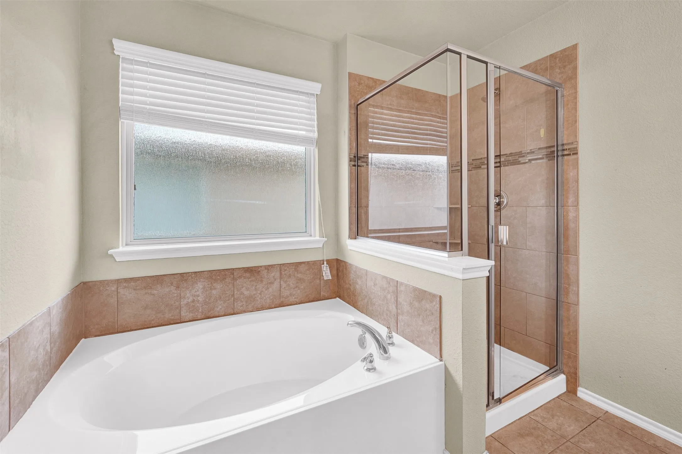 Bathroom featuring a built-in soaking tub with chrome fixtures, a tiled shower with a glass enclosure, and a privacy window with white blinds
