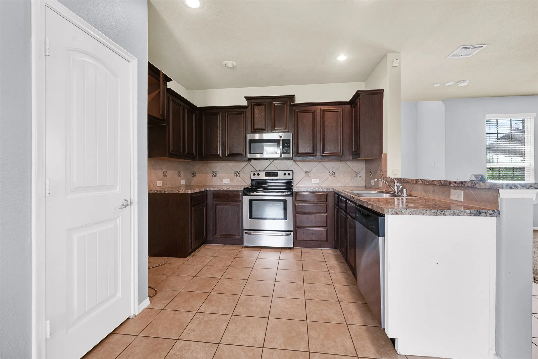 Kitchen featuring dark wood cabinetry, stainless steel appliances, tile flooring, and a breakfast bar with a stone-finish countertop