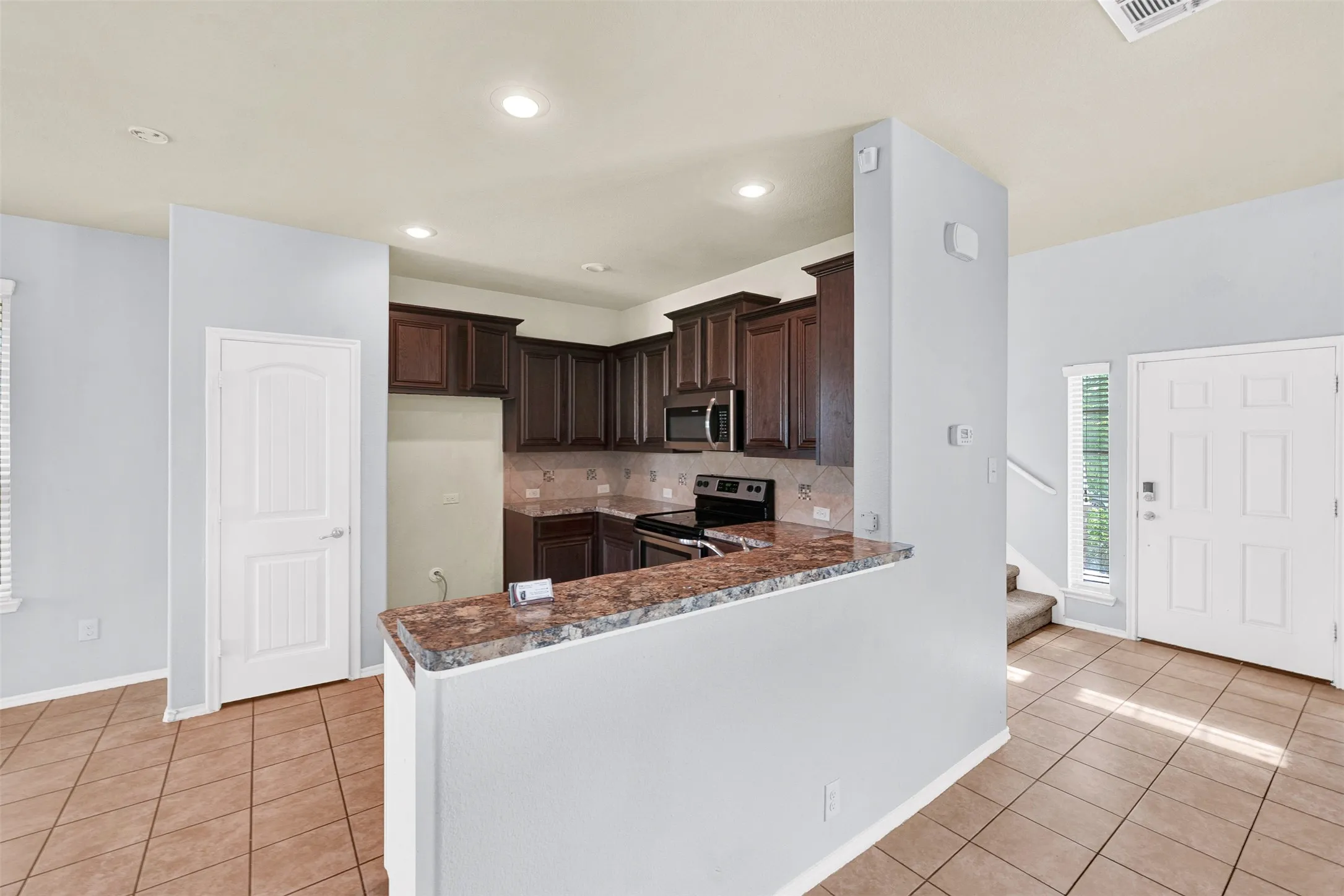 Kitchen featuring dark wood cabinetry, stainless steel appliances, recessed lighting, and a peninsula with a stone-finish countertop