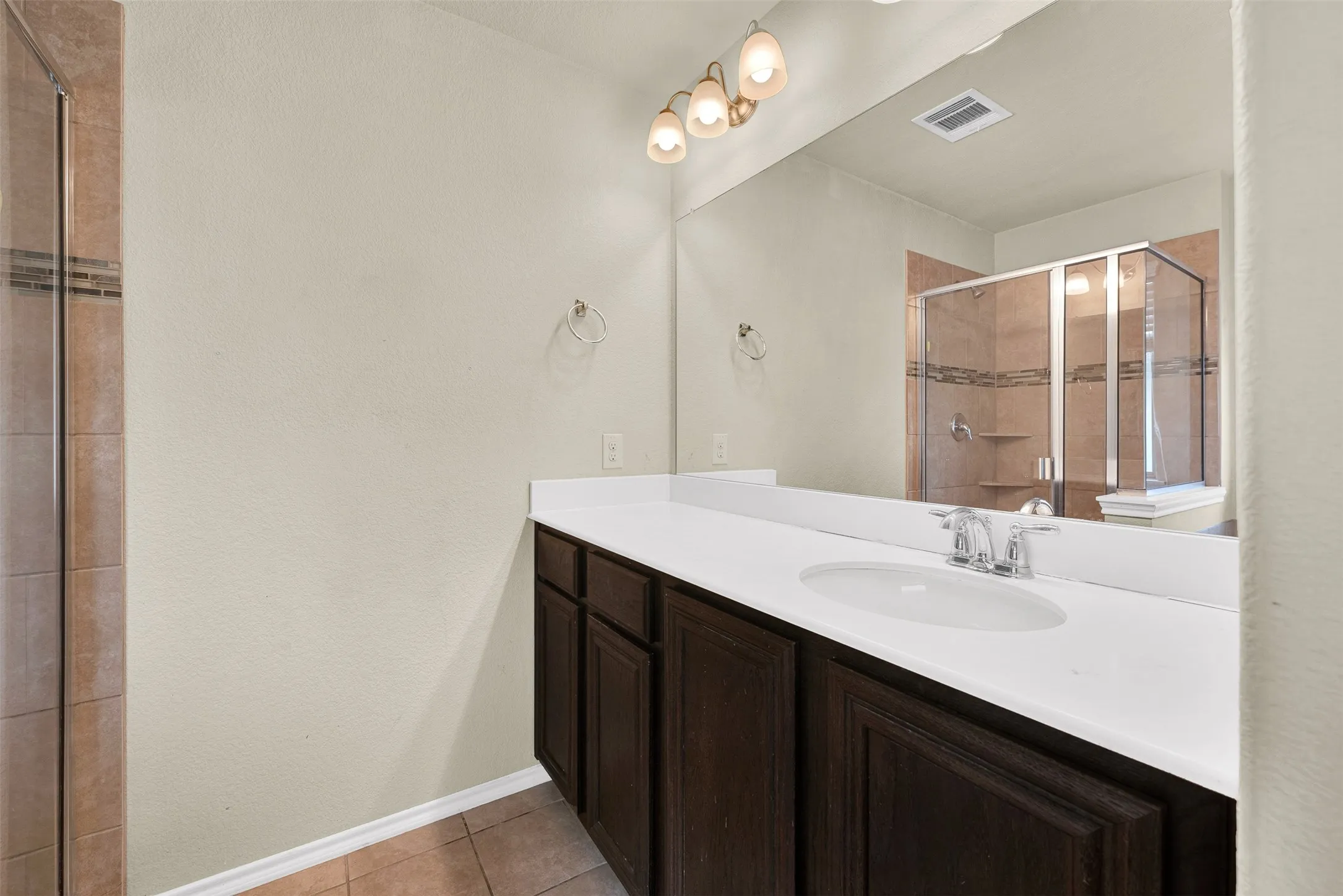 Bathroom vanity featuring a single integrated sink, chrome faucet, dark wood cabinetry, and a full-width mirror