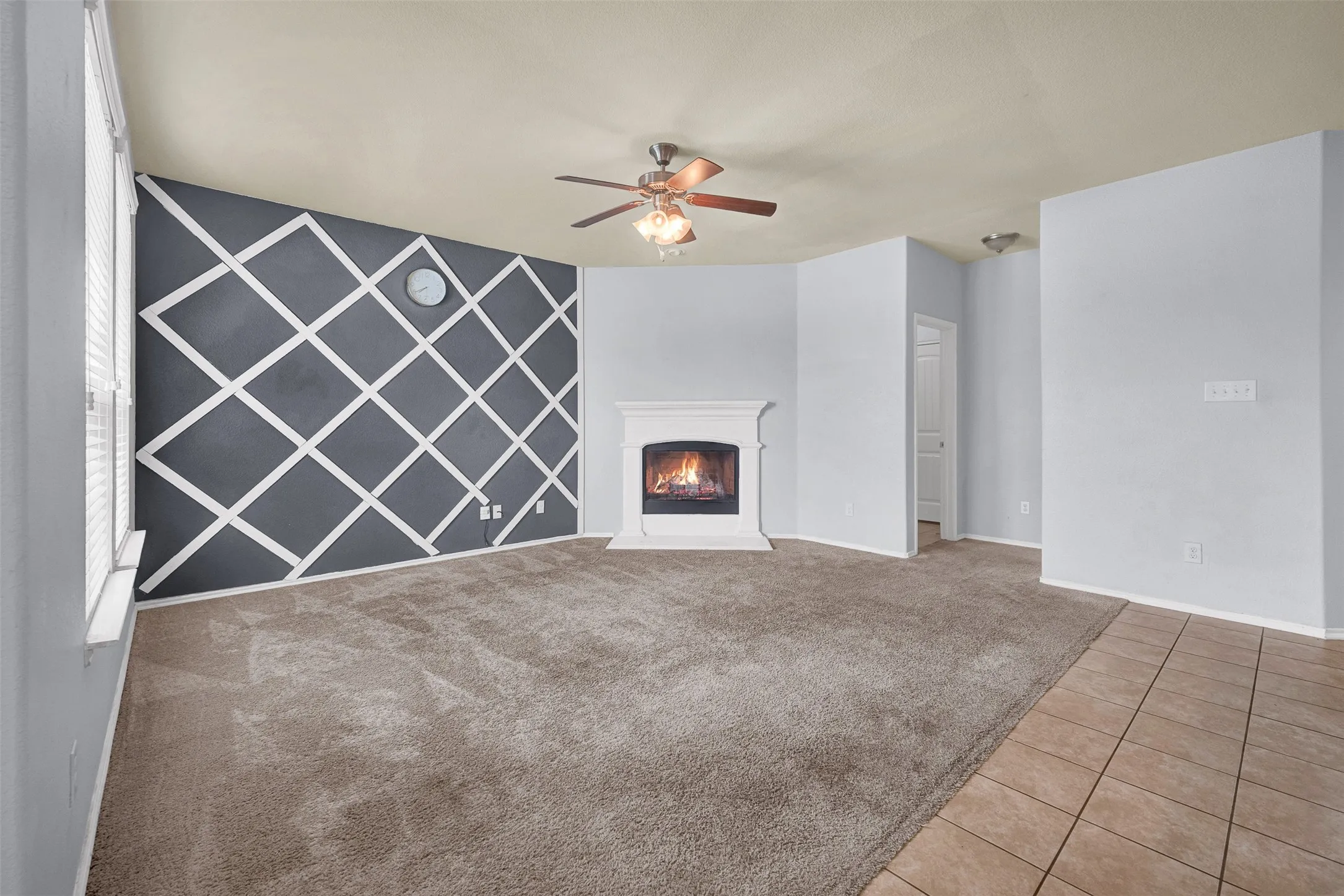 Living area featuring a decorative accent wall, a white fireplace surround, and a ceiling fan