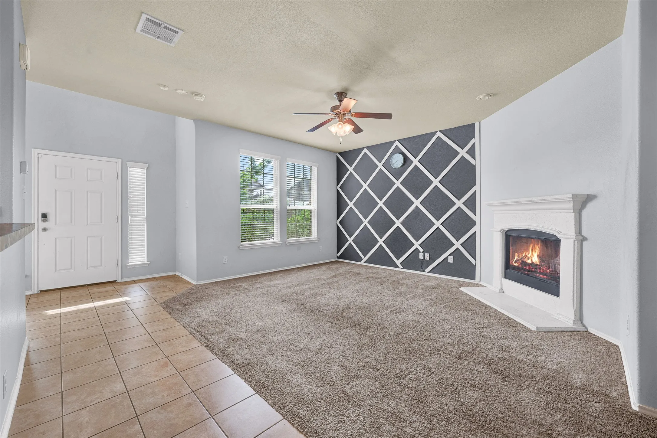 Living area featuring a fireplace with a white mantel, an accent wall with geometric paneling, and a ceiling fan with integrated lighting
