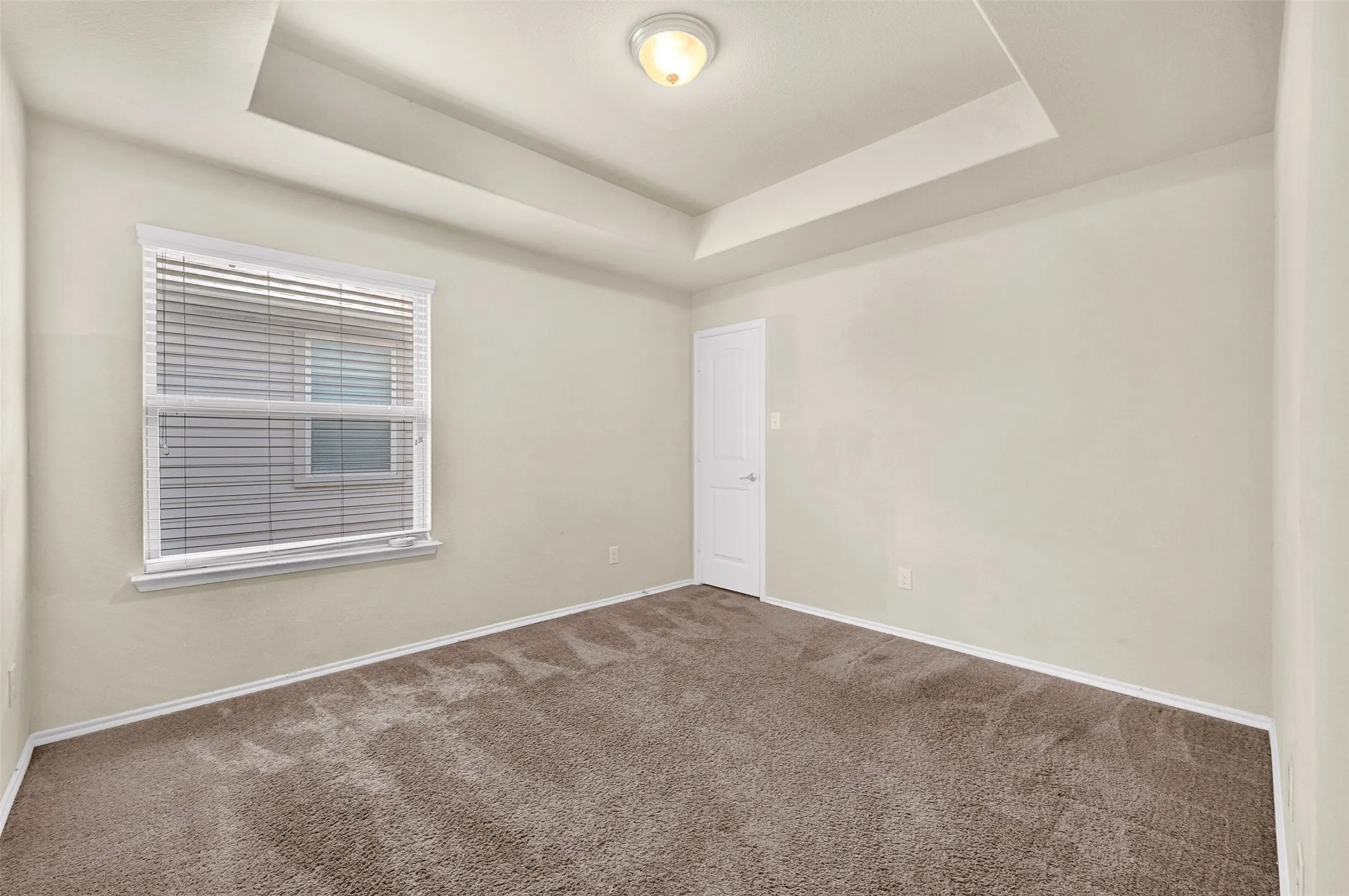 Bedroom featuring tray ceiling, light neutral wall paint, white trim, window with blinds, and brown carpet flooring