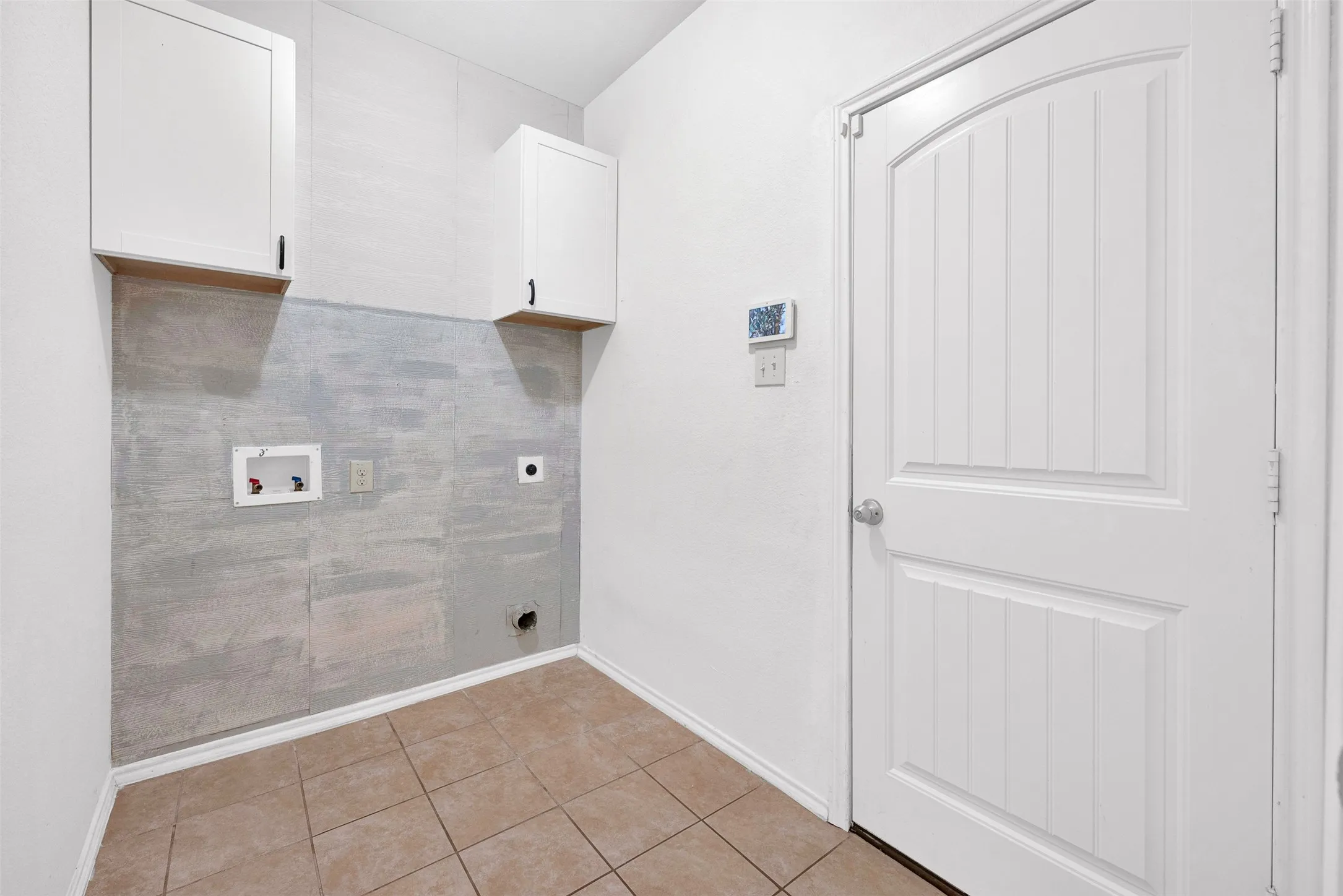 Utility room with two upper wall cabinets, tile flooring, and a white paneled door