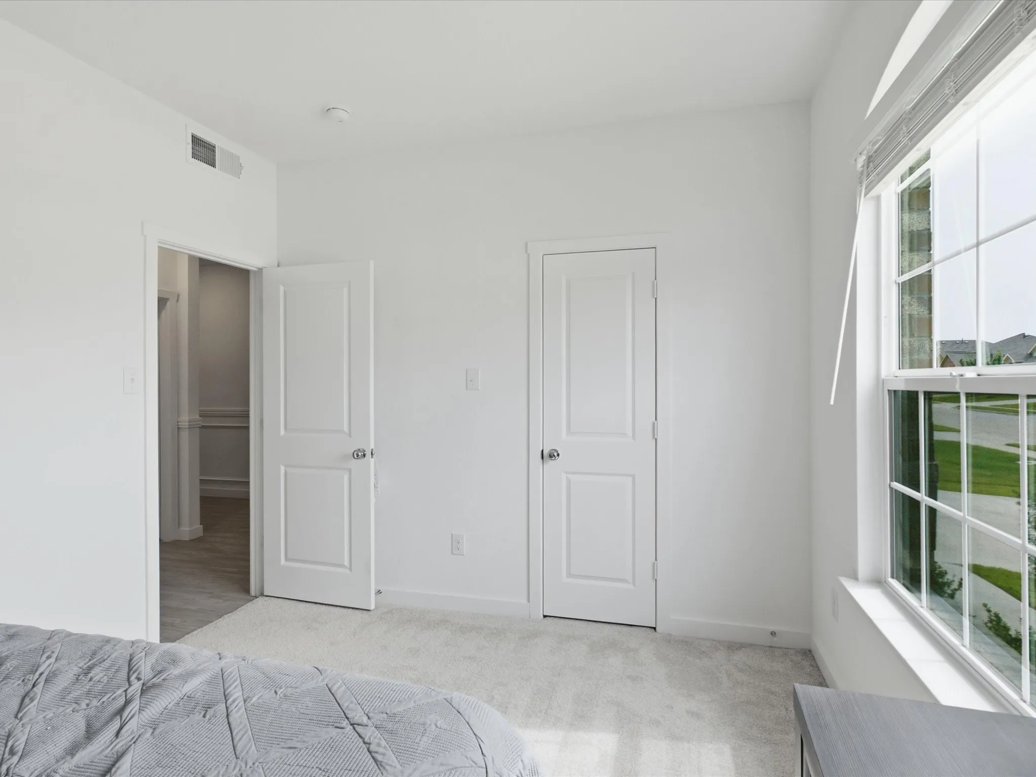 Bright room with white walls, light gray carpet, and a large window featuring white blinds
