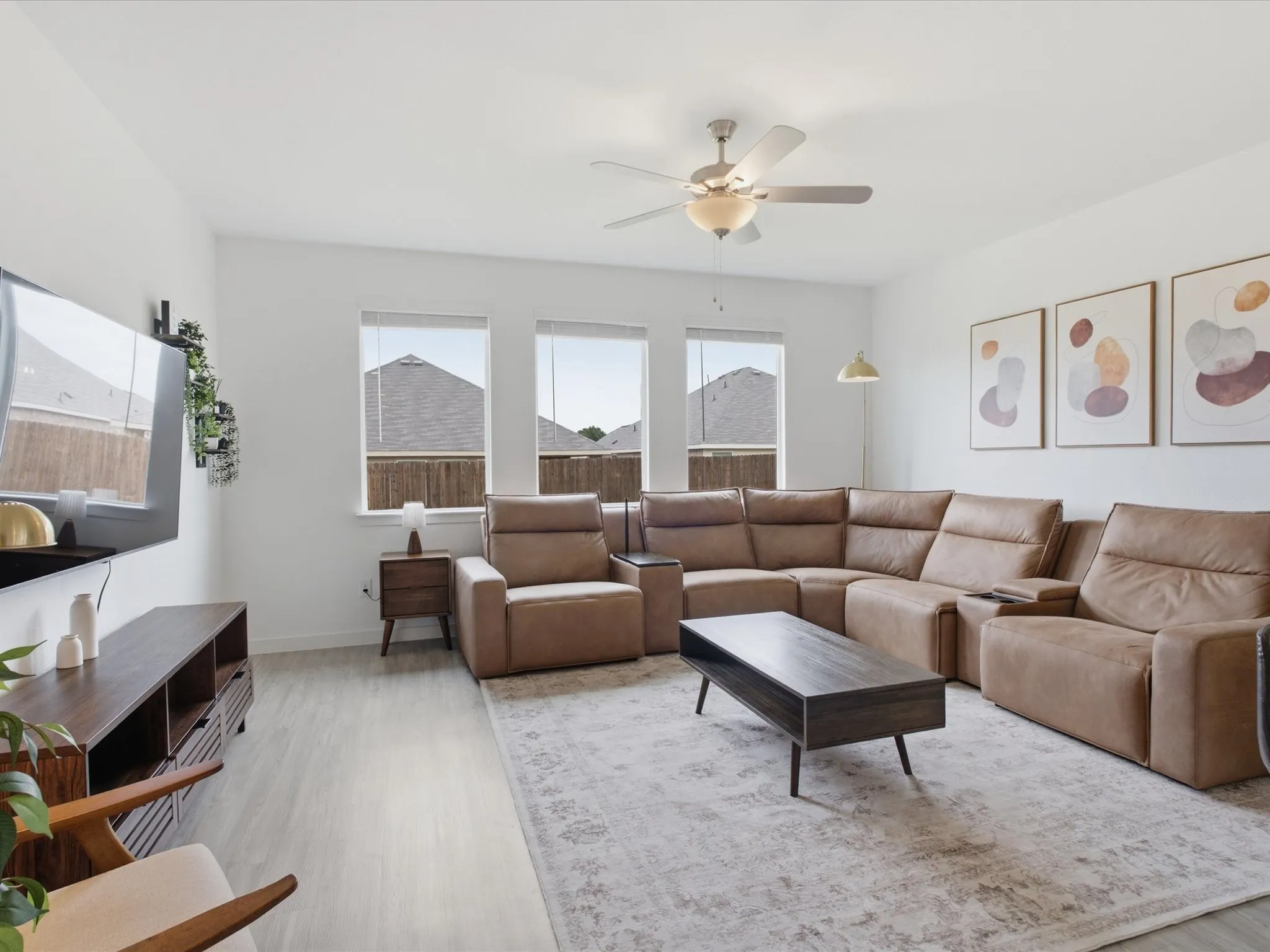 Spacious living area featuring light wood-finish flooring, white walls, and a ceiling fan with integrated lighting