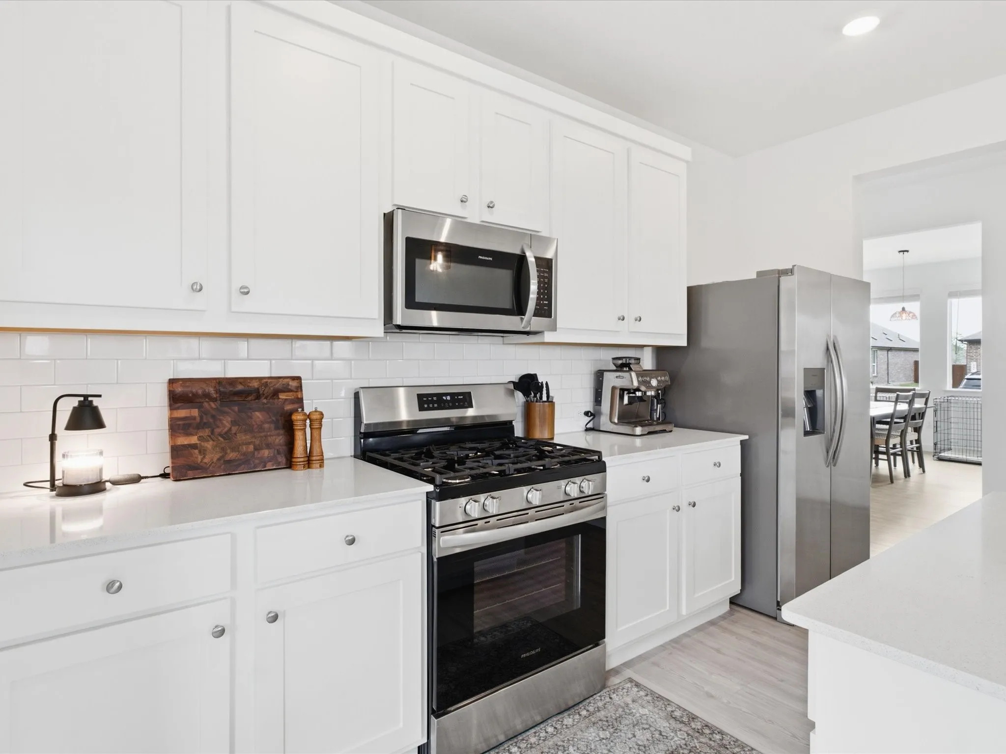 Contemporary kitchen featuring white shaker cabinetry, stainless steel appliances, white subway tile backsplash, and light wood-finish flooring