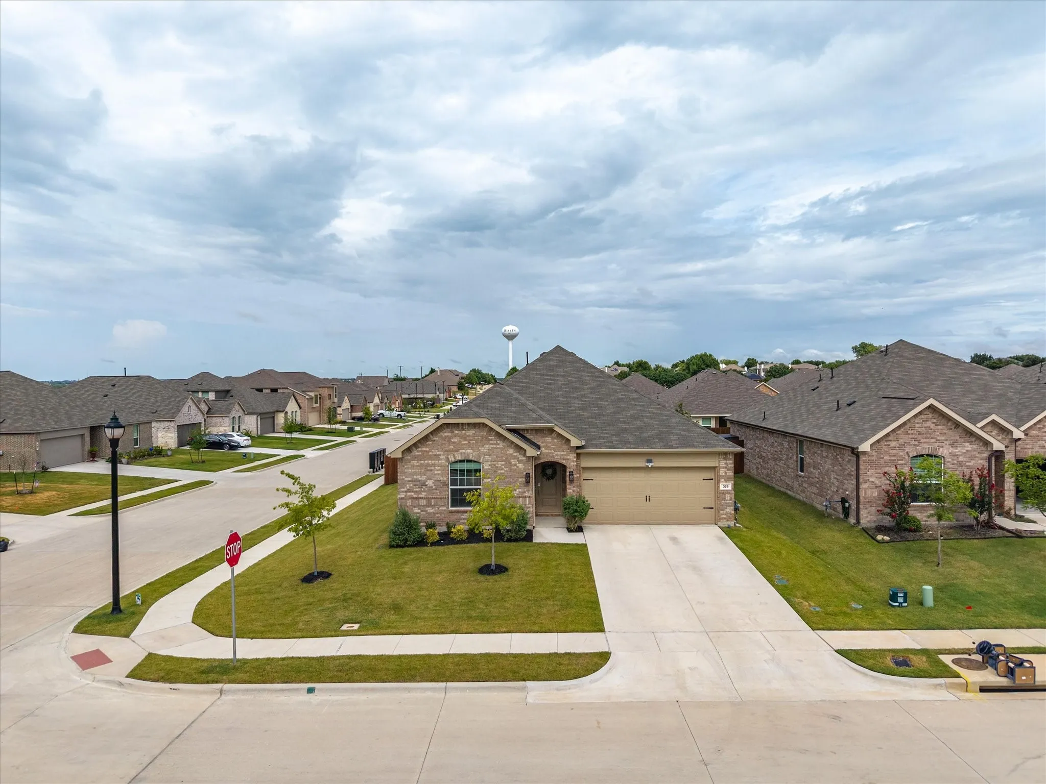 Single-story brick exterior home featuring an attached two-car garage, concrete driveway, and a manicured lawn