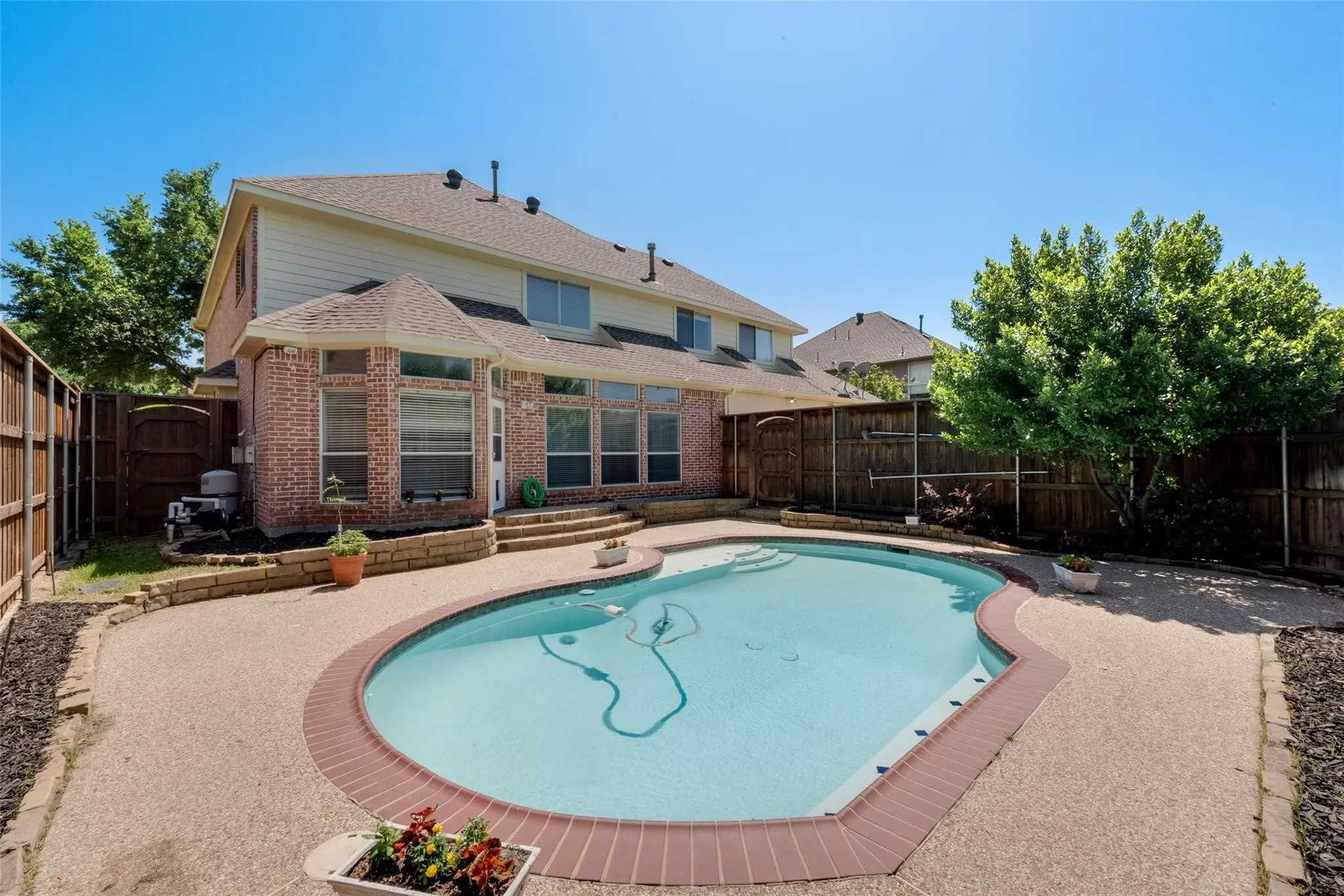 Freeform swimming pool with a surrounding aggregate concrete deck and brick coping