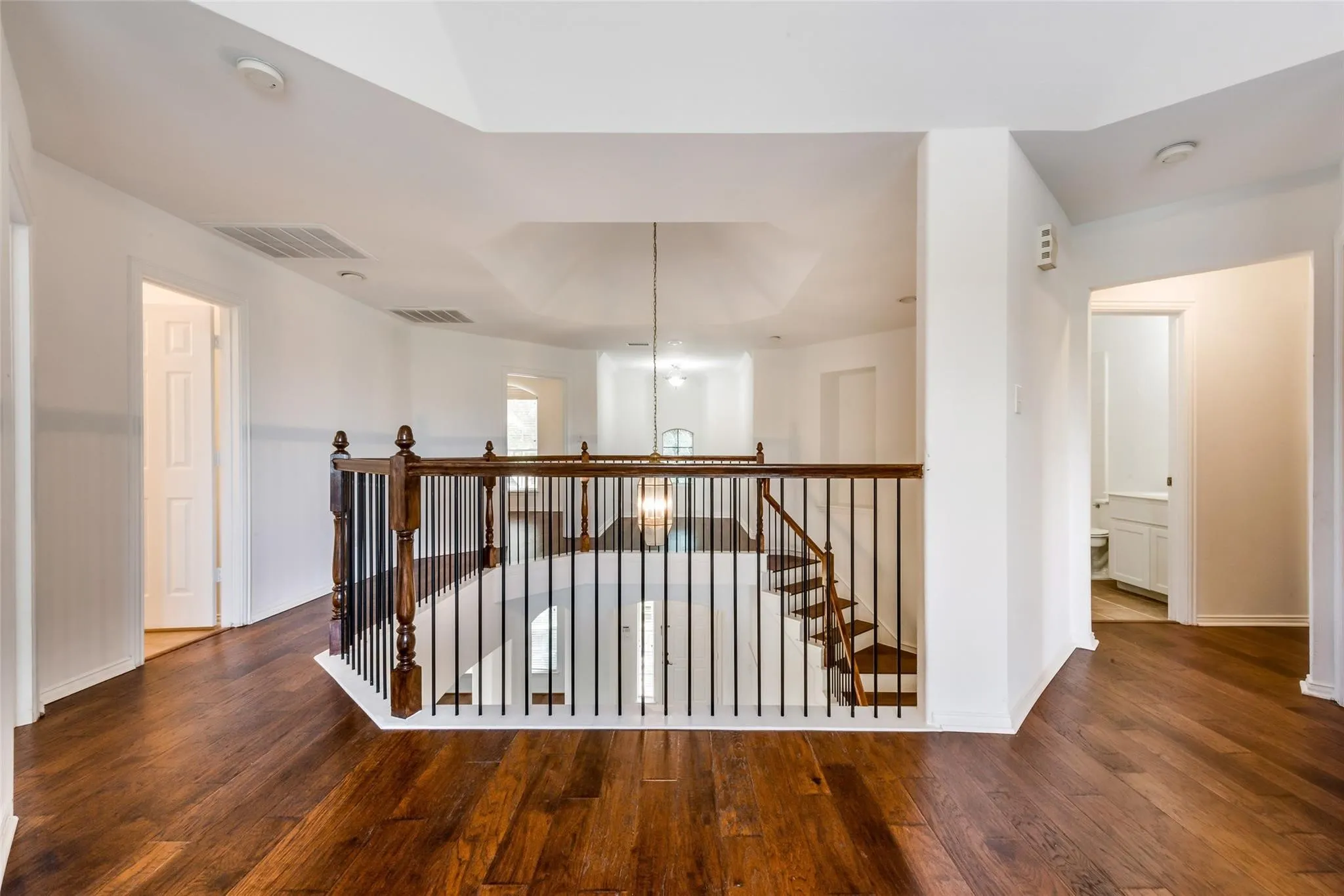 Upper level landing featuring rich wood-finish flooring, a dark wood and wrought iron staircase, white walls, and a tray ceiling
