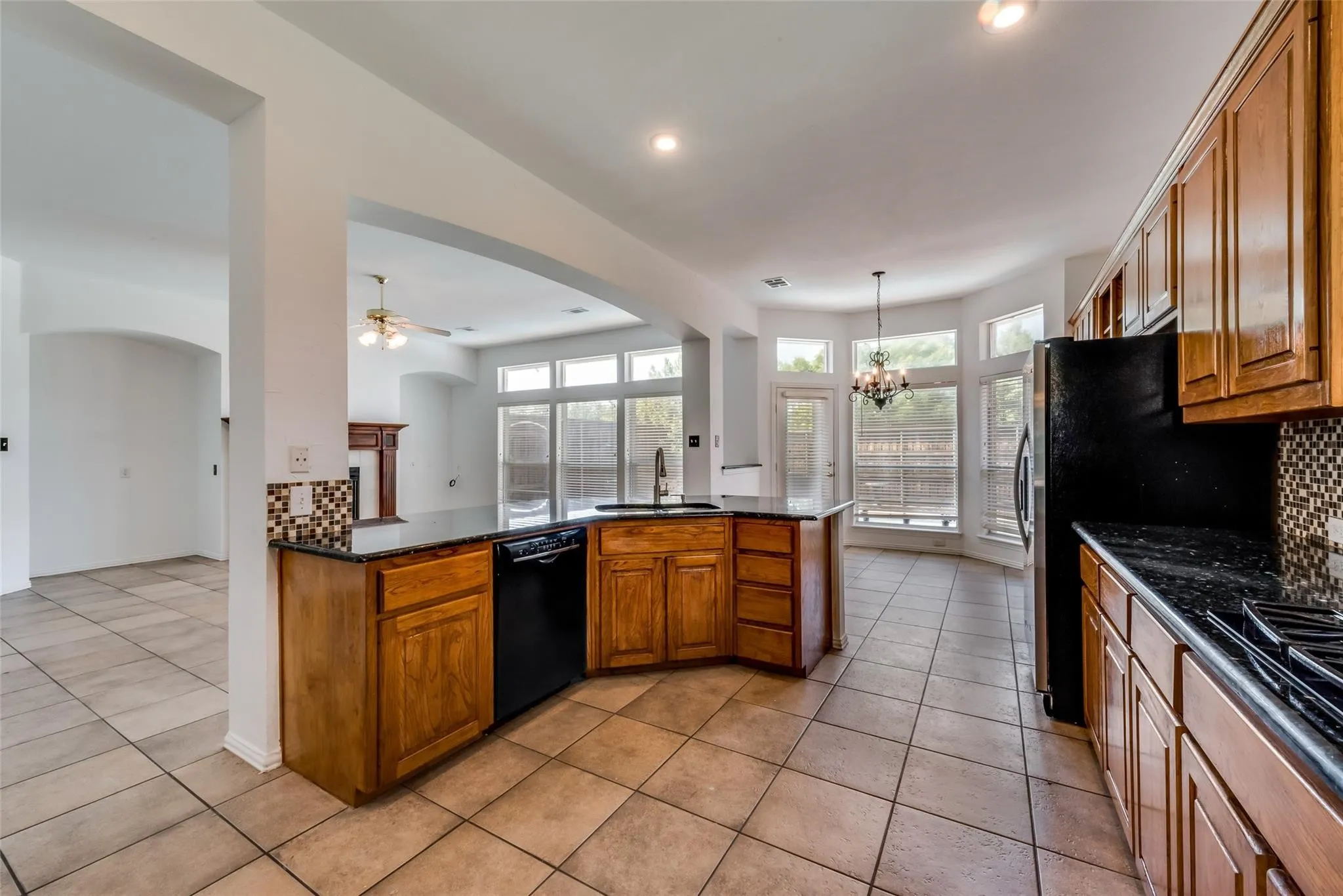 Kitchen featuring wood cabinetry, black appliances, dark countertops, and mosaic tile backsplash
