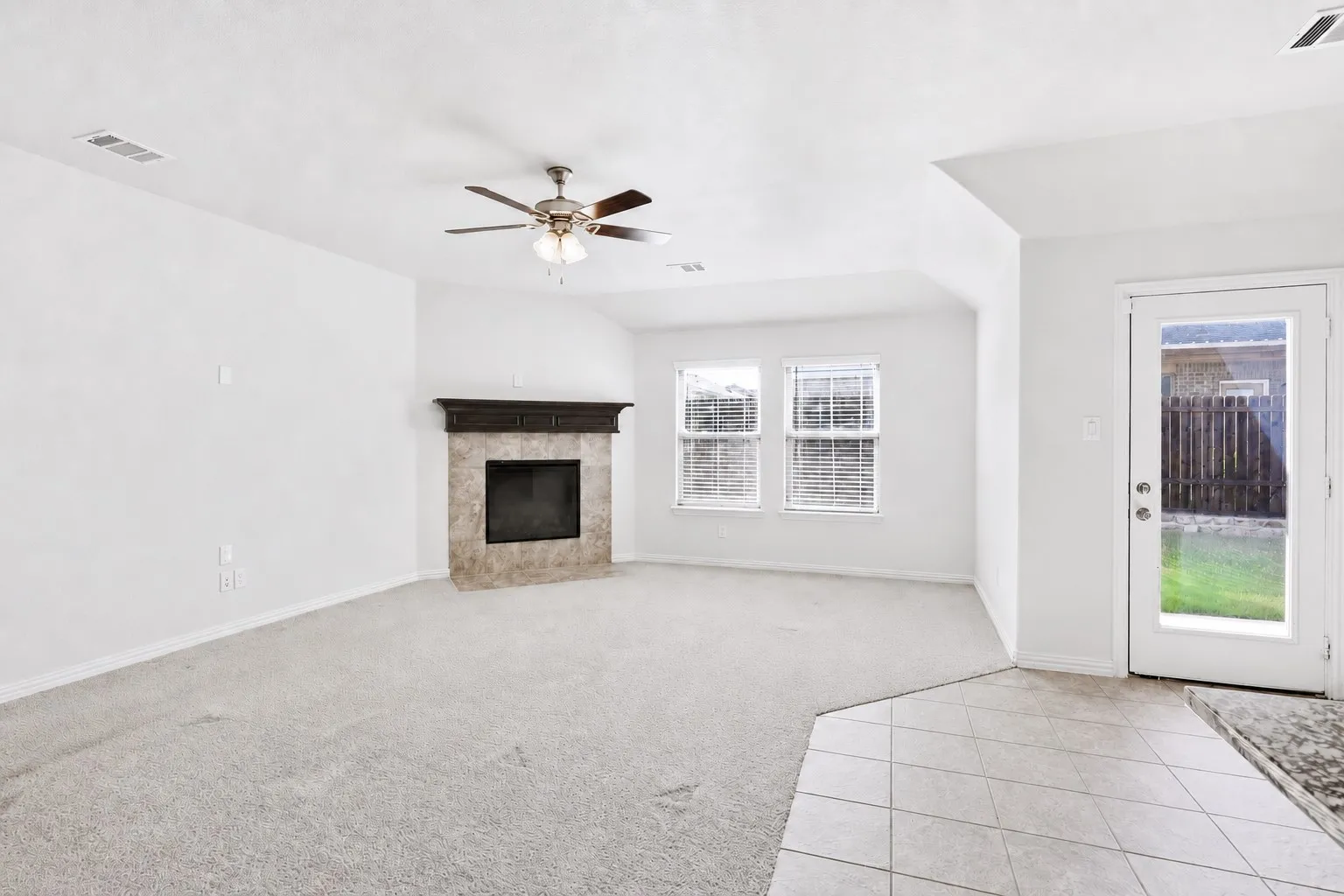 Living area with a tile-surround fireplace, dark wood mantel, and a ceiling fan with integrated lighting