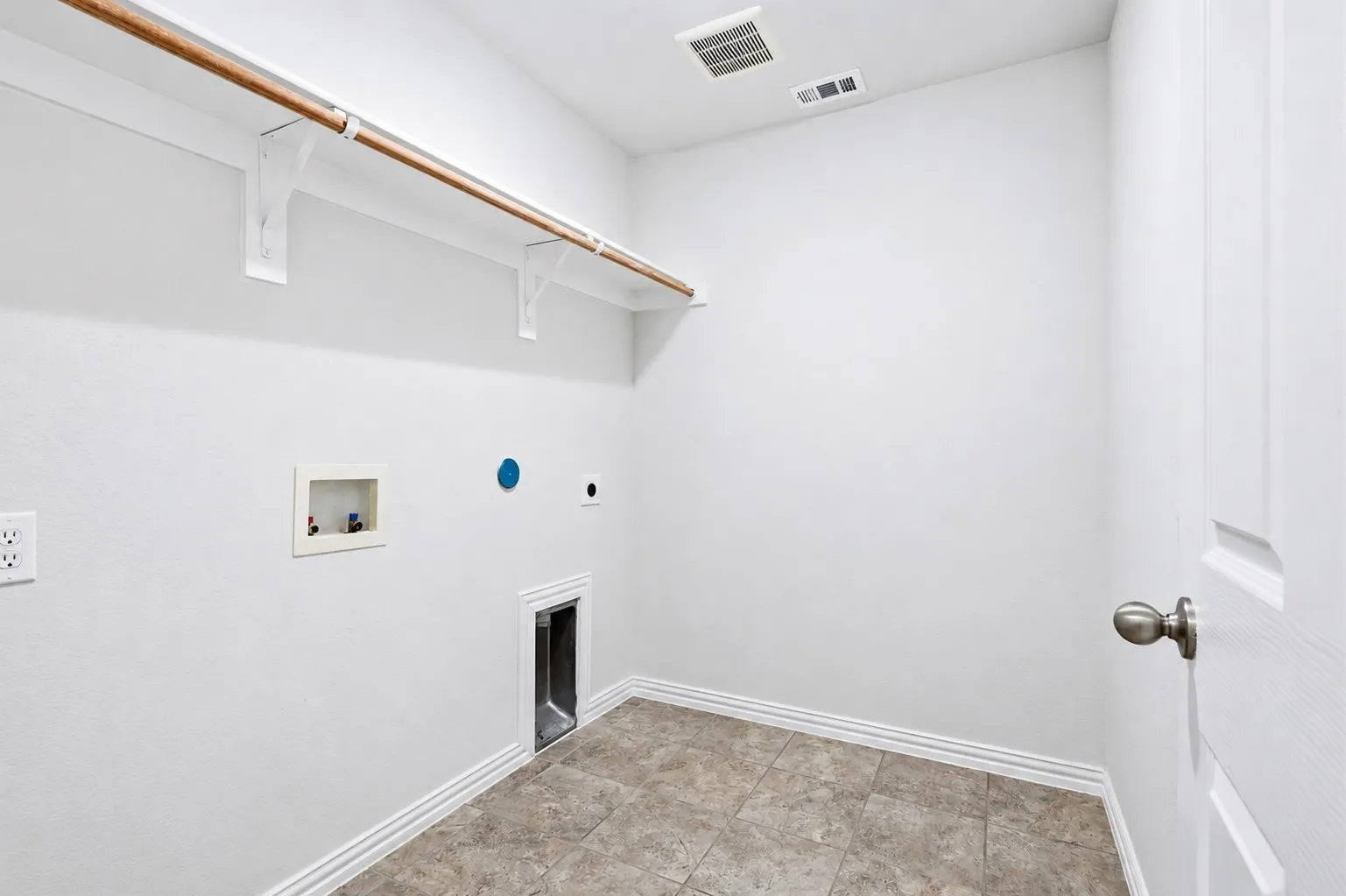 Dedicated utility space featuring tile flooring, white walls, and a built-in shelf with a clothing rod