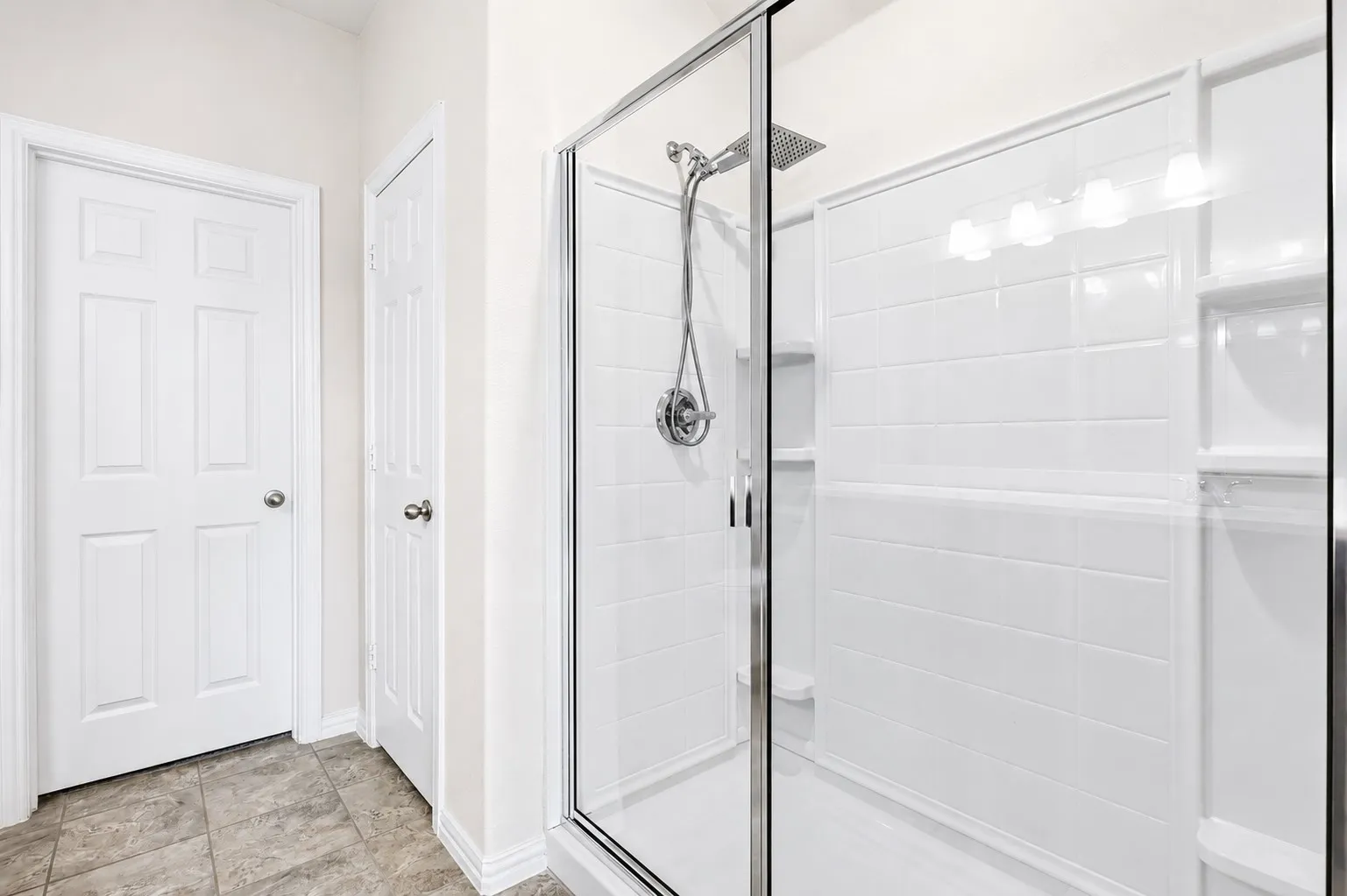 Glass-enclosed shower featuring a rainfall showerhead, handheld shower fixture, built-in shelving, and white subway tile-patterned wall surround