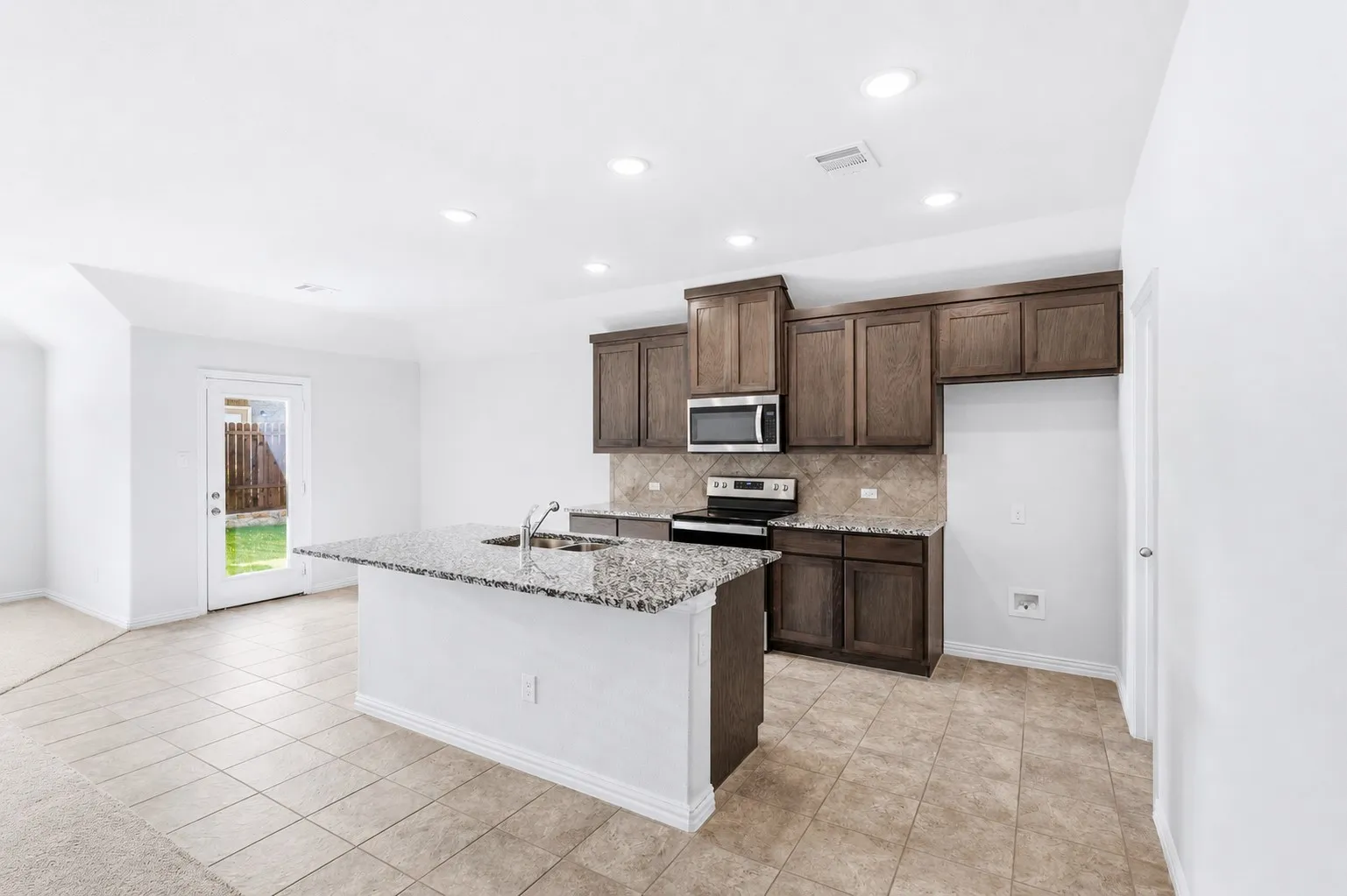 Kitchen featuring an island with a built-in sink, granite countertops, wood-finish cabinetry, and stainless steel appliances