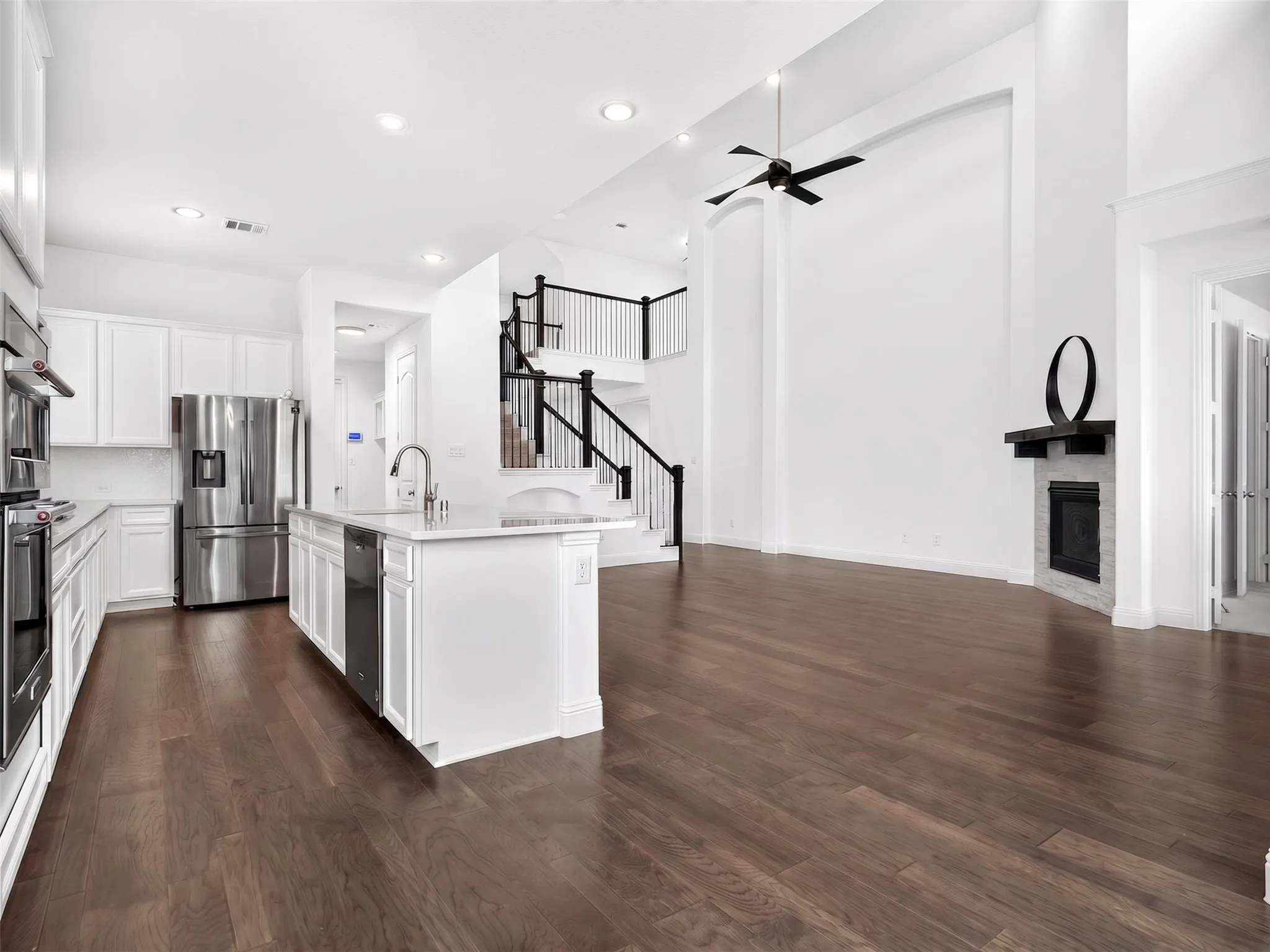 Open-concept living space featuring wood-finish flooring, a two-story ceiling, and a fireplace with a dark mantel