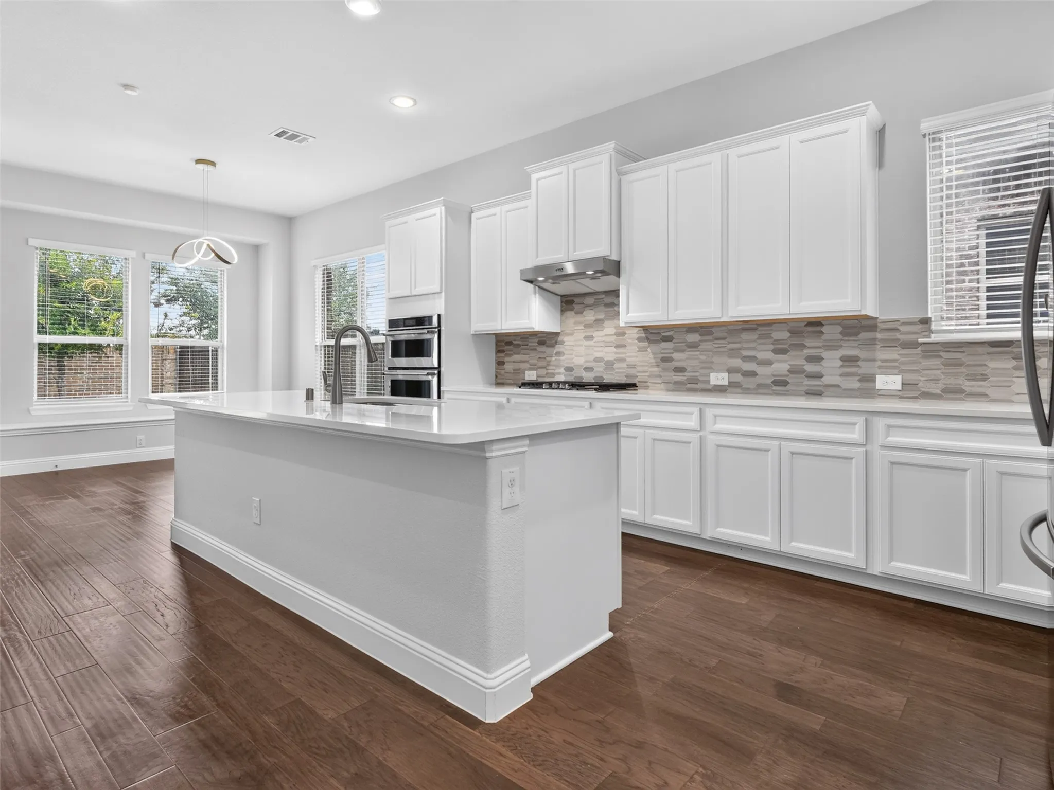 Modern kitchen with wood-finish flooring, a central island featuring a gooseneck faucet, white shaker-style cabinetry, a multi-tone tile backsplash, and built-in stainless steel appliances