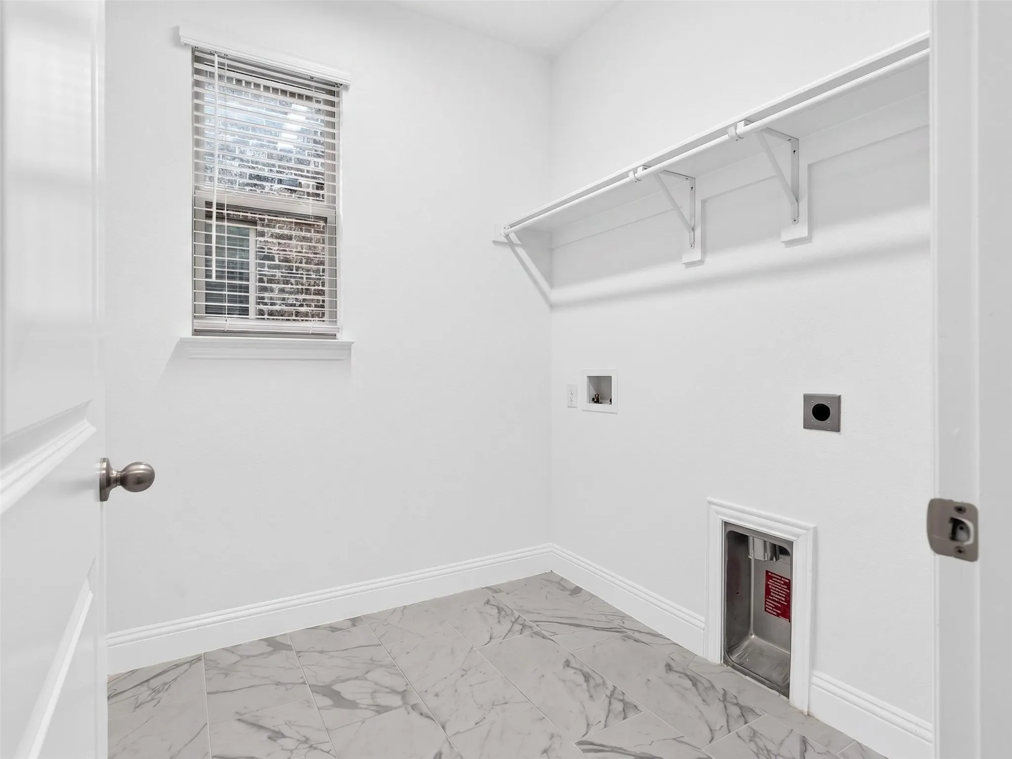 Utility room with marble-style flooring, natural light, and convenient washer-dryer hookups plus storage shelf