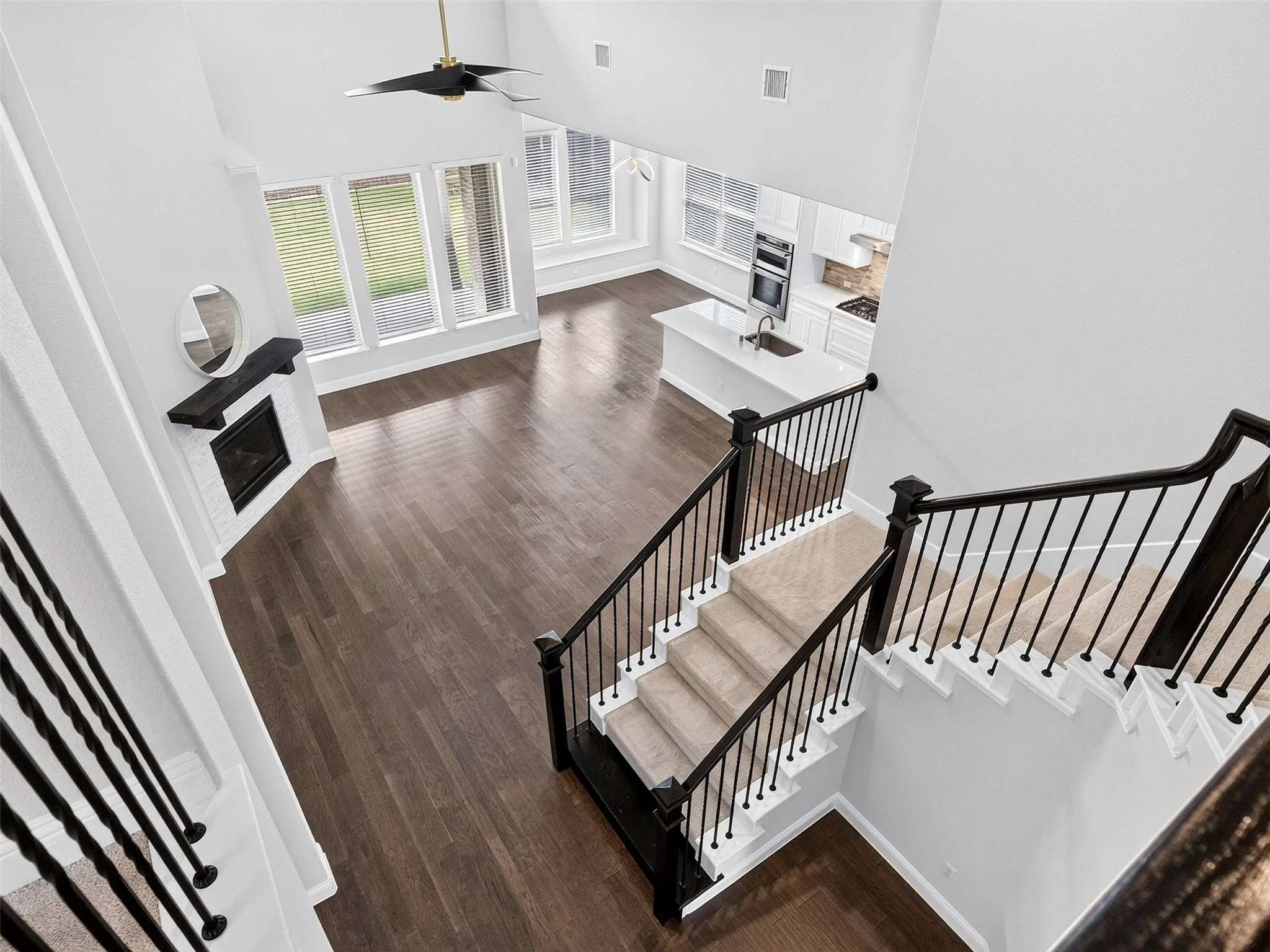 Two-story living area featuring wood-finish flooring, a white brick fireplace with a dark wood mantel, and large windows
