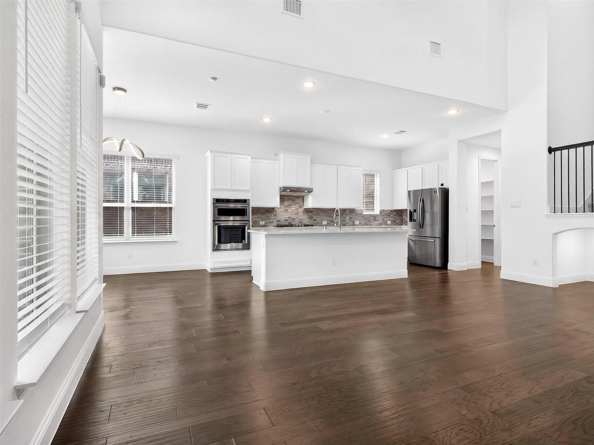 A bright, modern open-concept kitchen and living area featuring dark hardwood floors, white cabinetry, stainless-steel appliances, a large quartz island, and abundant natural light
